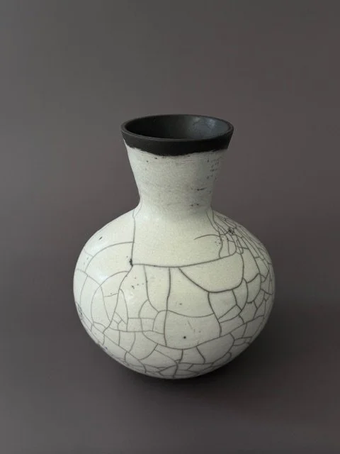 A white ceramic vase with black crackle design and a black interior, set against a plain gray background.