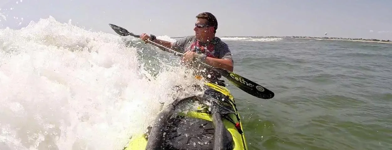 Person kayaking in the ocean on a sunny day, wearing sunglasses and a life jacket.