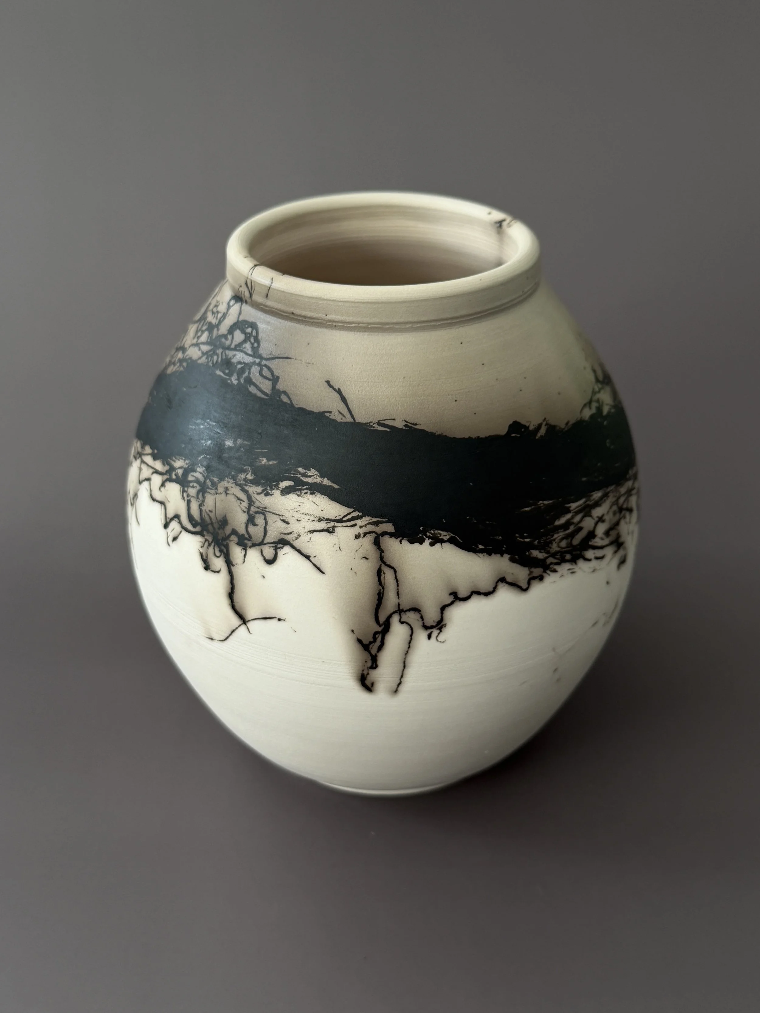 A ceramic vase with a round shape, featuring a beige and black abstract design created by horsehair.