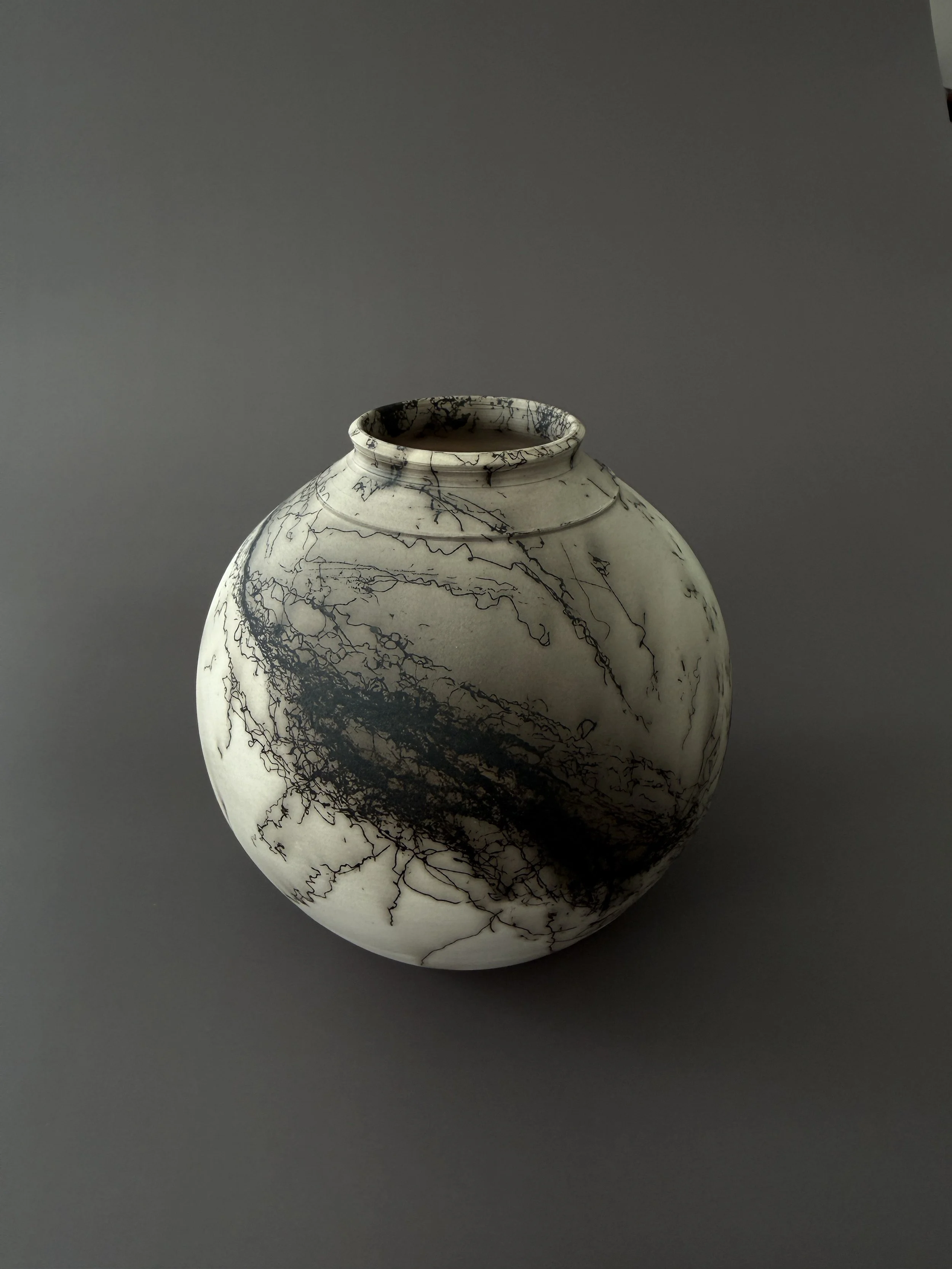 A white ceramic vase with black crackle patterns, set against a plain gray background.