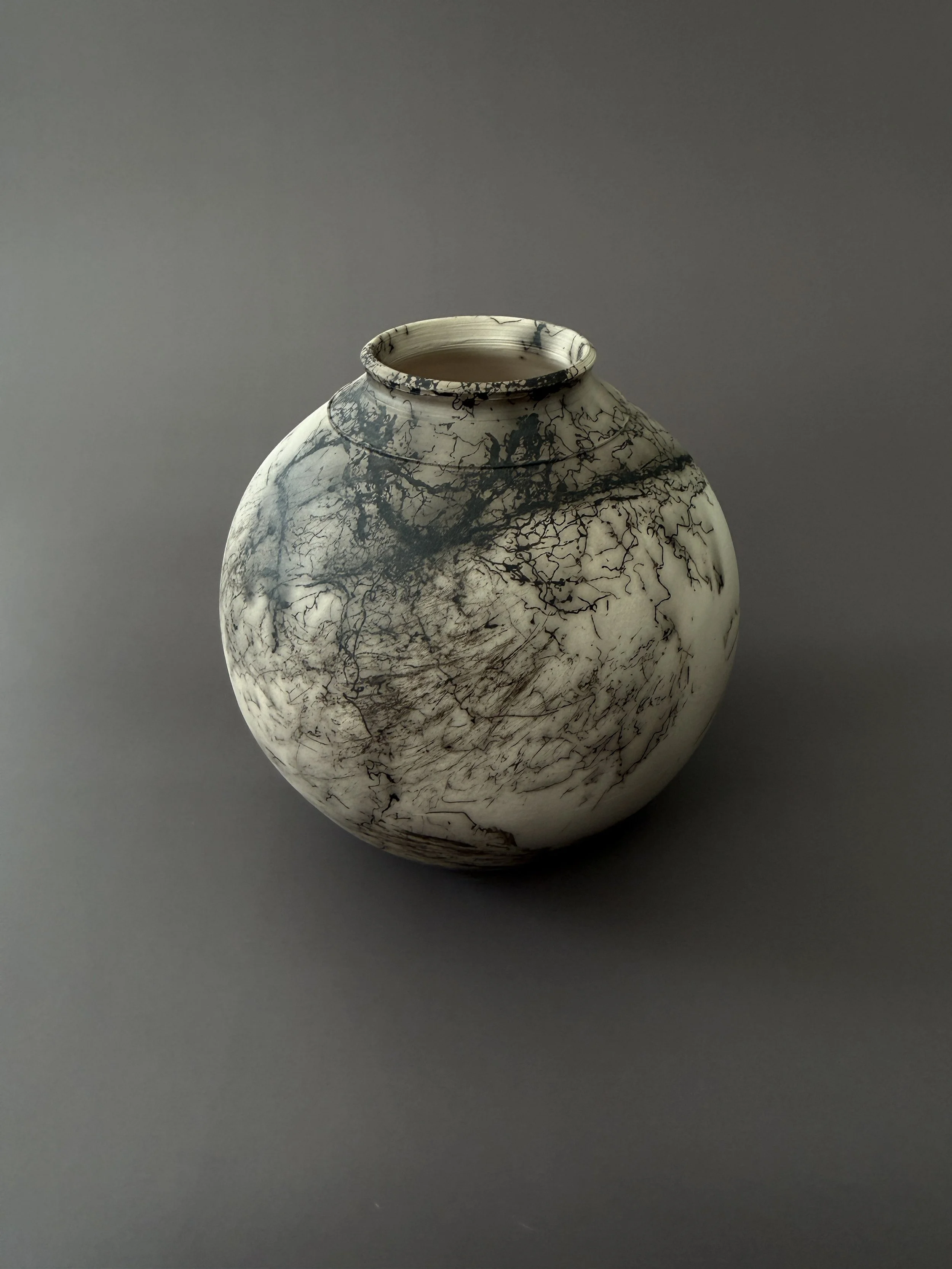 A round ceramic vase with a black and white marbled pattern on a gray background.