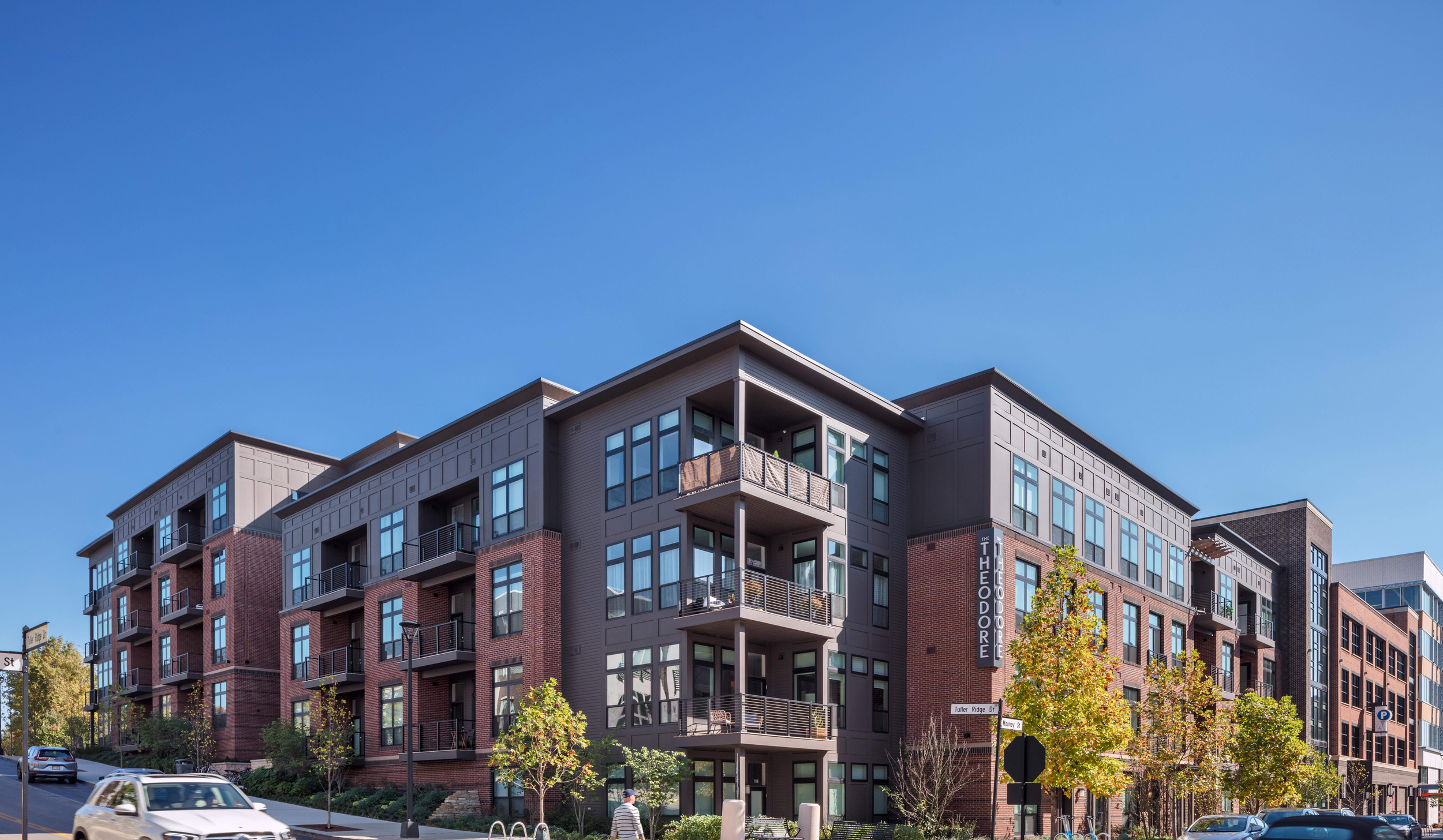 Modern apartment building with brick and gray siding, multiple balconies, and large windows, under a clear blue sky.