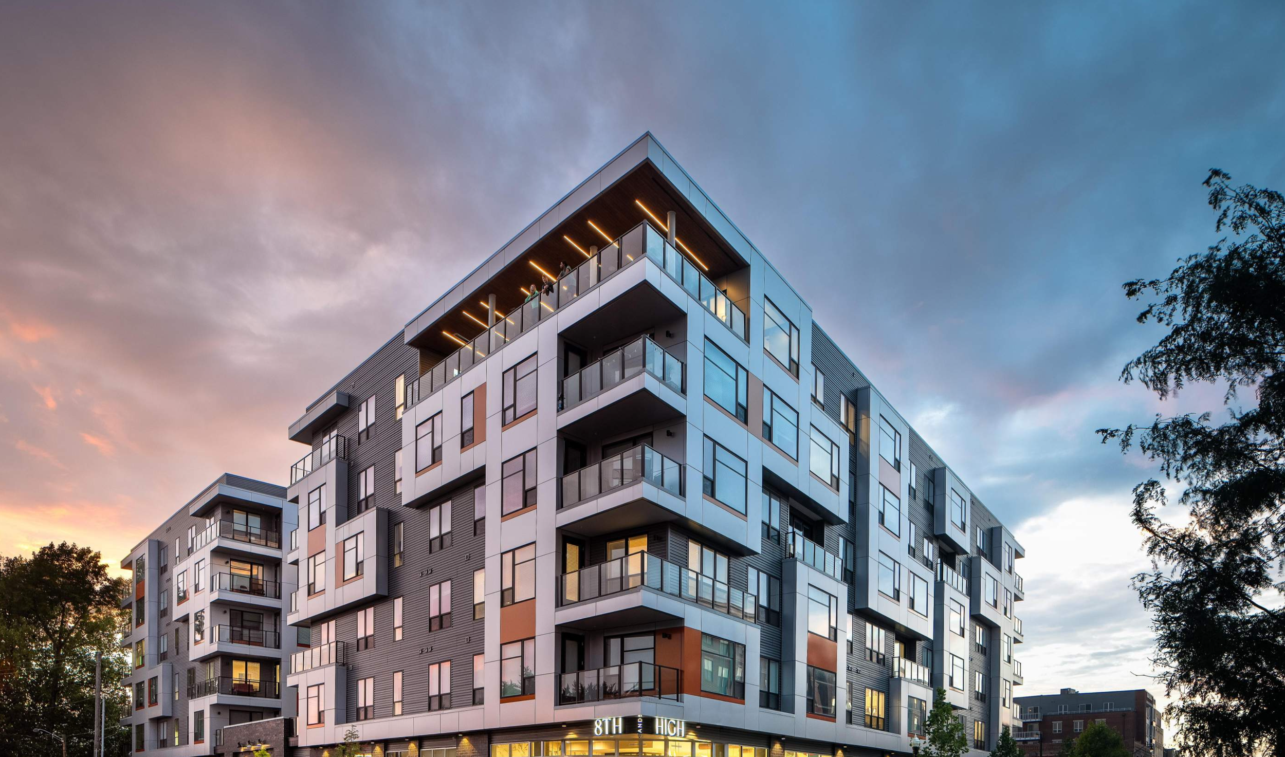 Modern multi-story residential building with glass balconies at sunset or dusk.