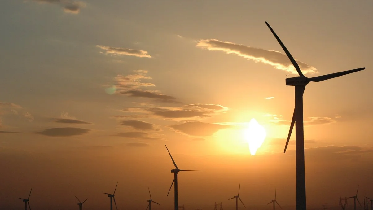 A sunset over a wind farm with multiple wind turbines.