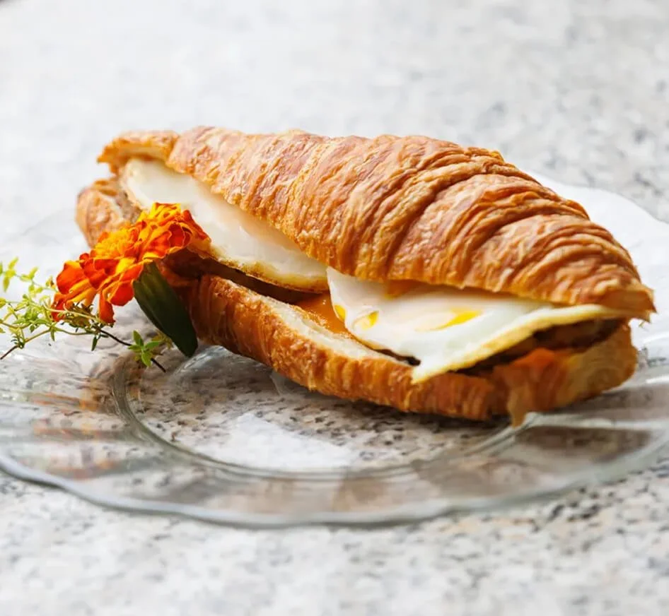 Croissant sandwich with fried egg, on a glass plate with a flower decoration.