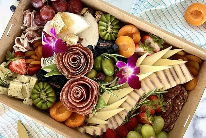 A cheese and charcuterie tray with grapes, strawberries, apricots, sliced cheese, cured meats, and edible flowers
