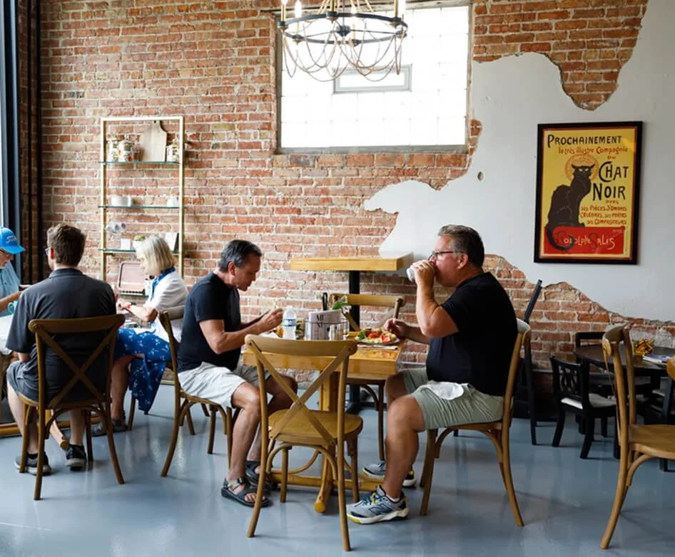 People dining in a restaurant with exposed brick walls, a chandelier, and a vintage poster on the wall.