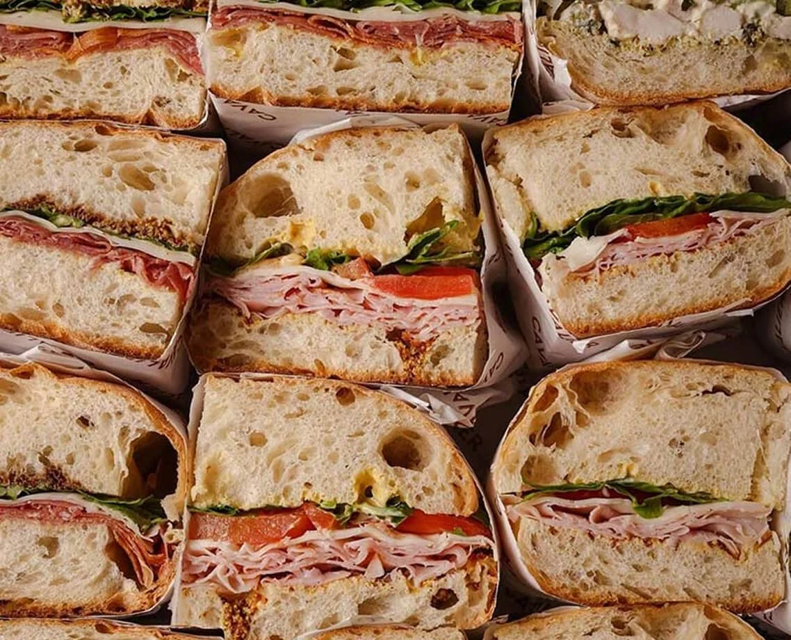 Close-up of sliced sandwiches with ham, tomato, lettuce, and bread.