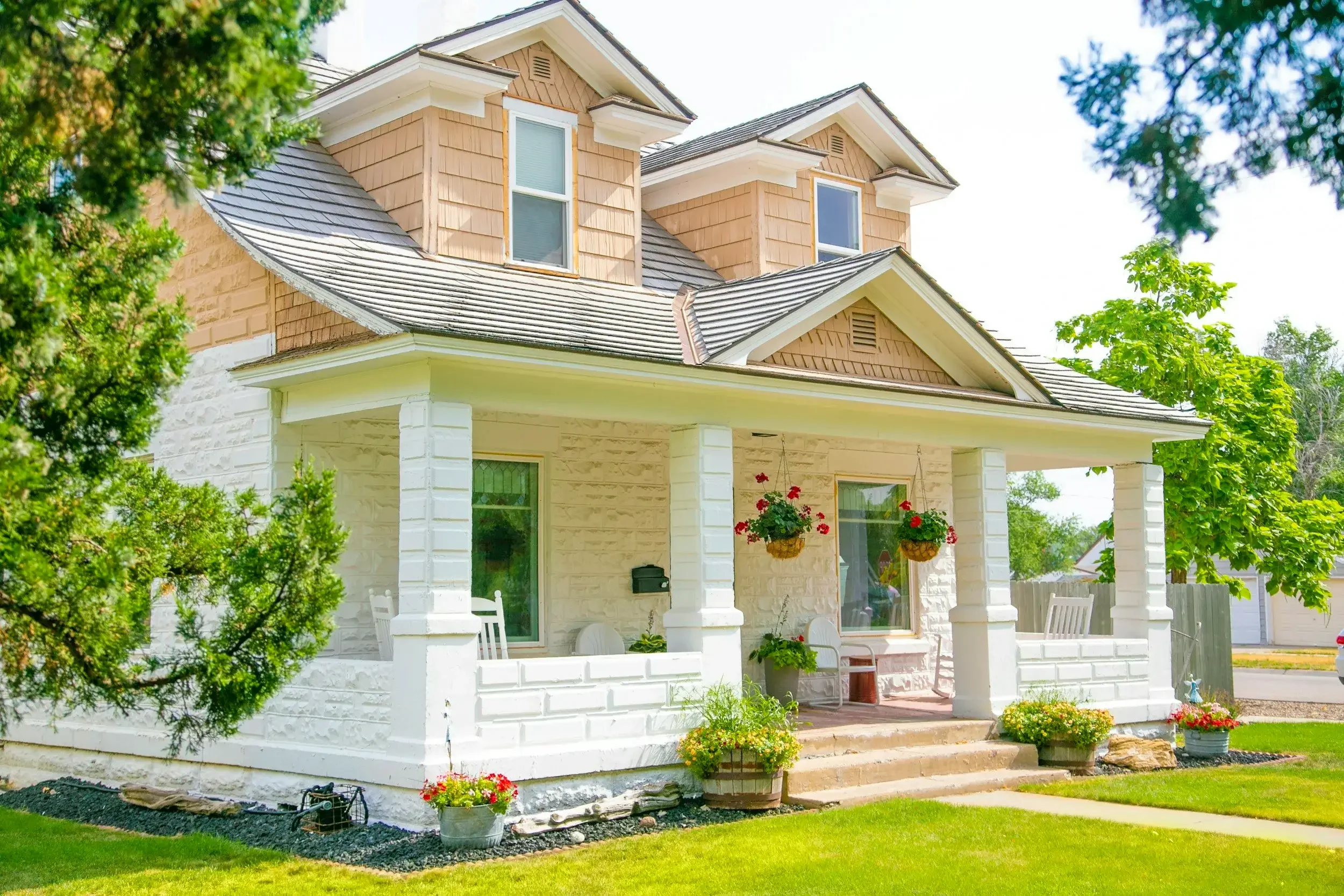Light-colored two-story house with dormer windows, a shingle roof, and a covered front porch.