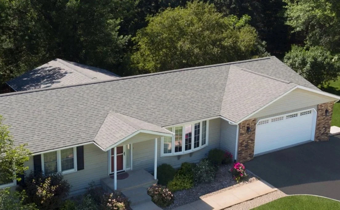 Single-story home with gray roof, front porch, garage, and landscaped yard.