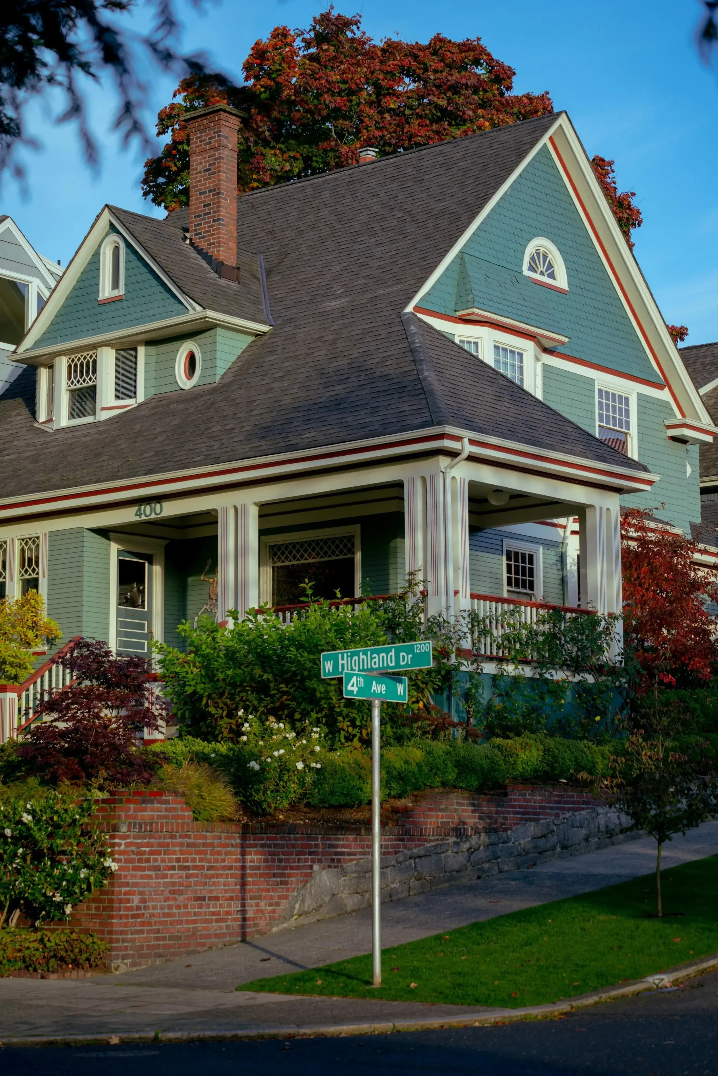 Green house with steep shingle roof gables, a brick chimney, and a covered porch.