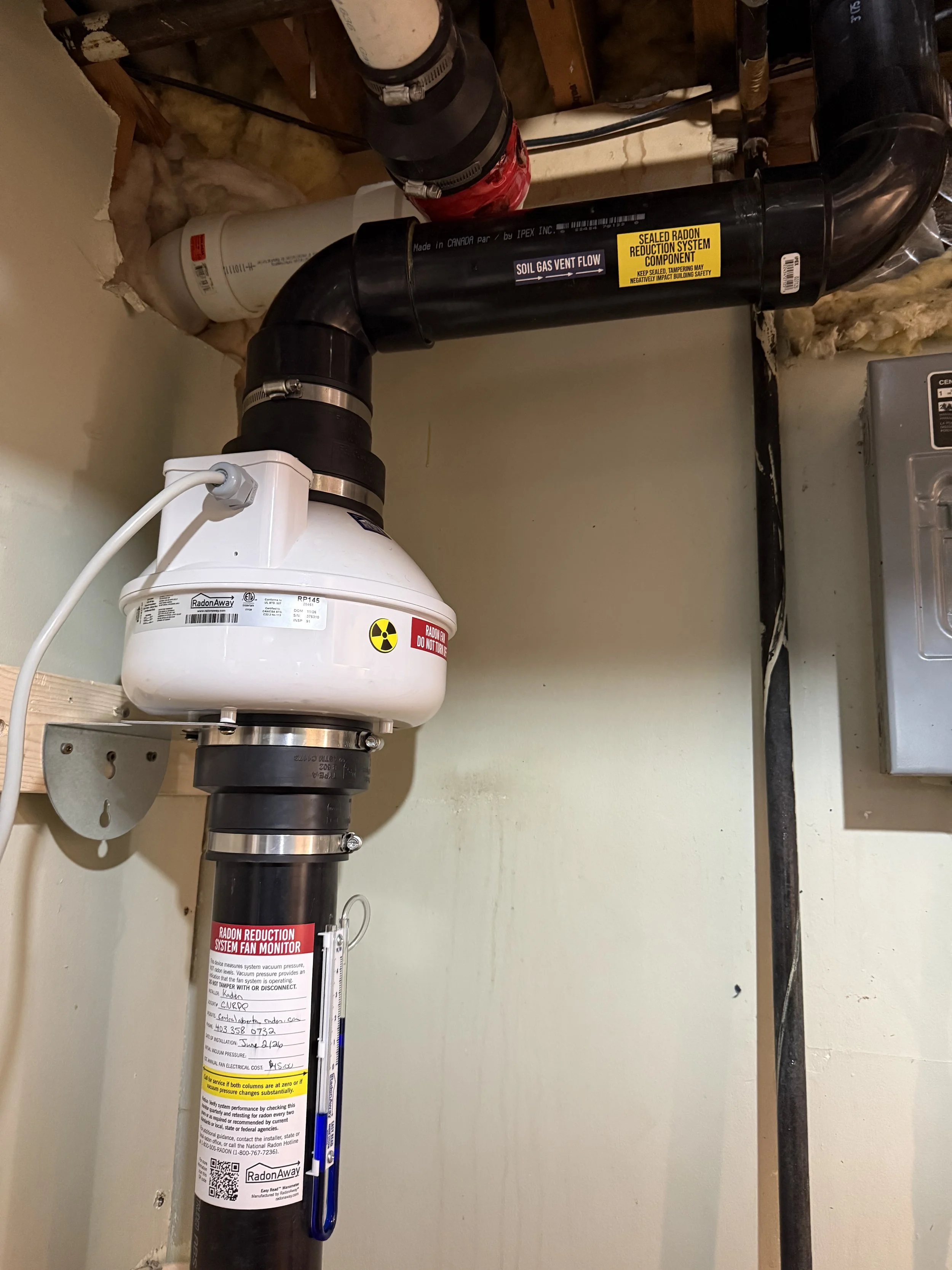 A gas ventilation system with labels and a inspection tag attached to black pipes in a utility or furnace room.