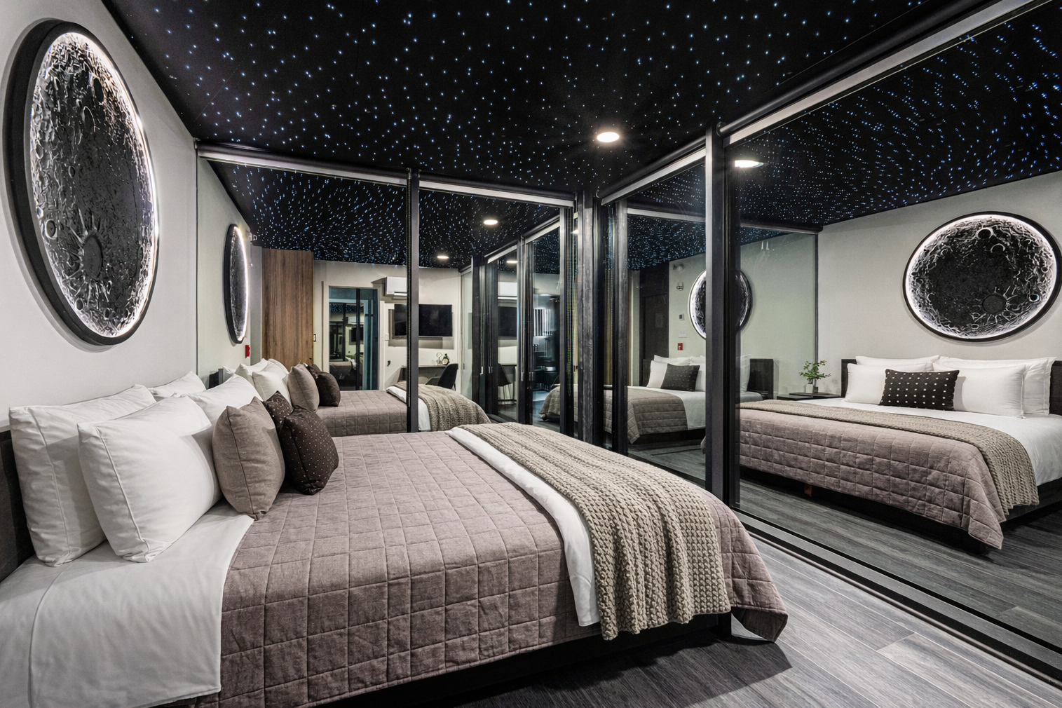 Modern hotel room with two beds, mirrored wall, moon phase artwork, starry ceiling, and sliding glass doors.