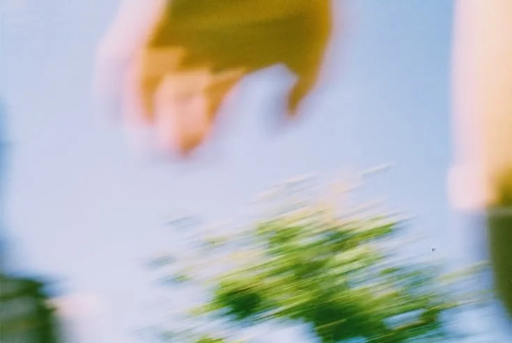 Blurred image of a person hanging upside down outdoors, with greenery and sky in the background.
