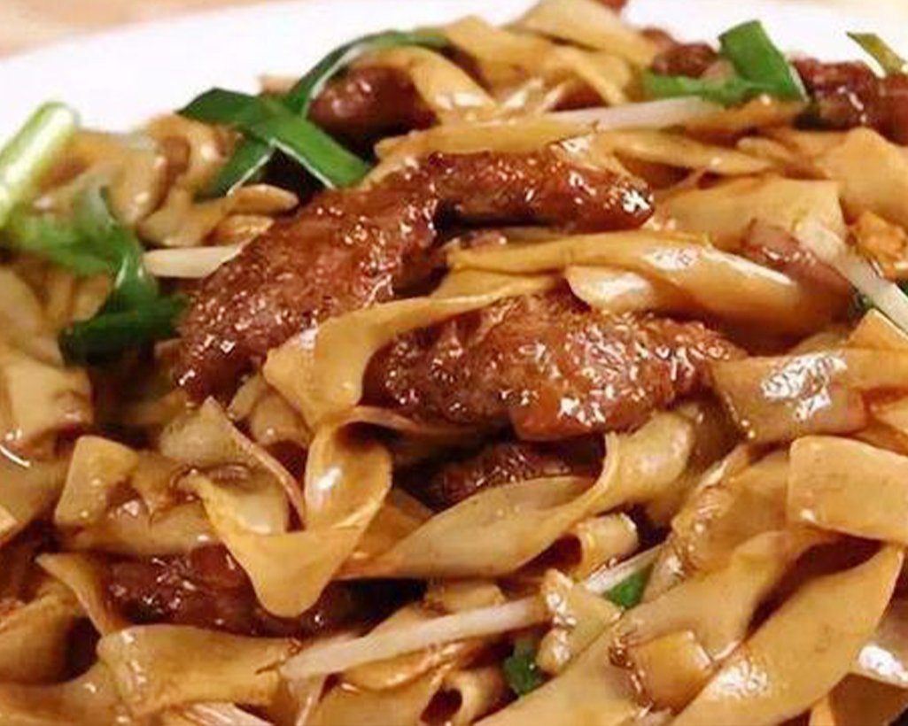 Close-up of stir-fried noodles with beef, green onions, and vegetables.
