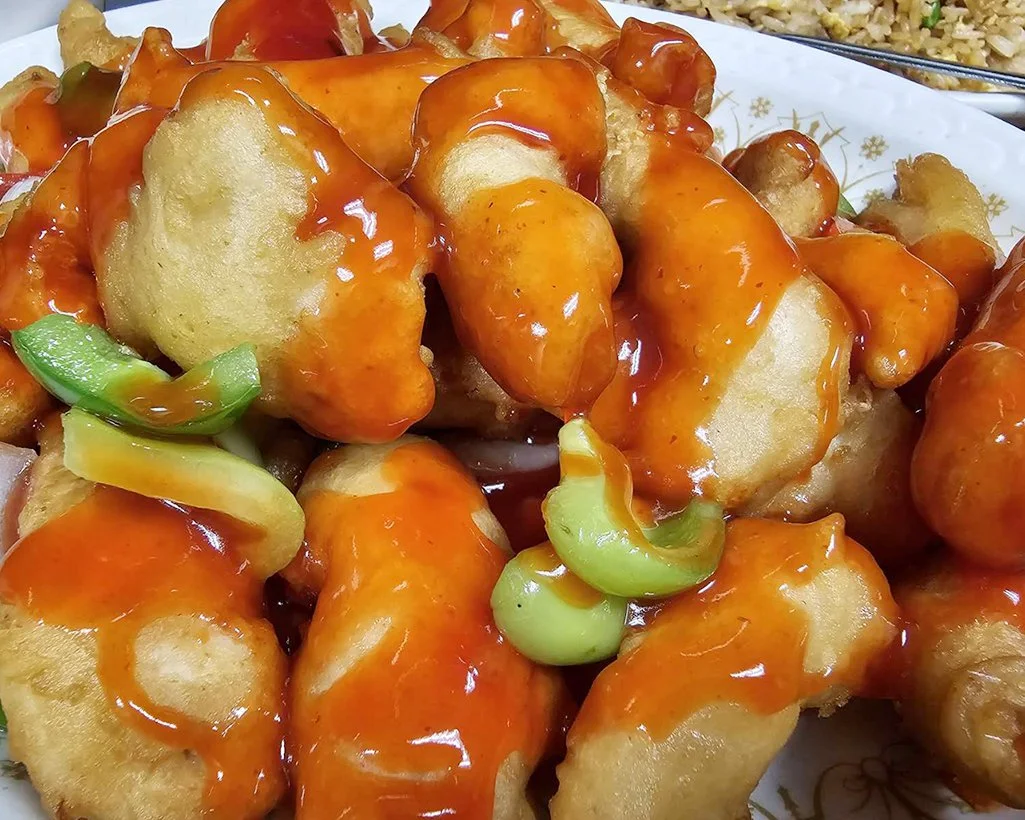 Deep-fried battered shrimp drizzled with orange sauce, garnished with green onions.