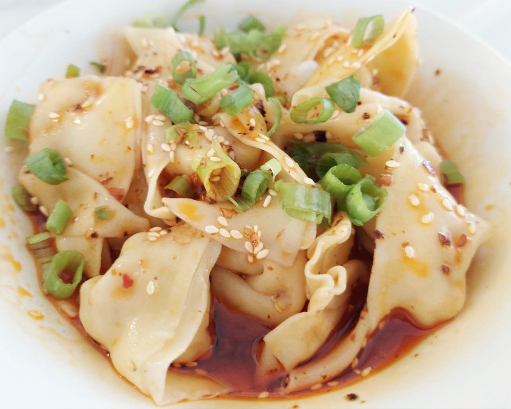 Close-up of dumplings topped with chopped green onions and sesame seeds in a soy-based sauce.