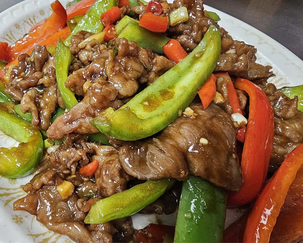 Stir-fried beef with red, green, and orange bell peppers on a decorative white plate.