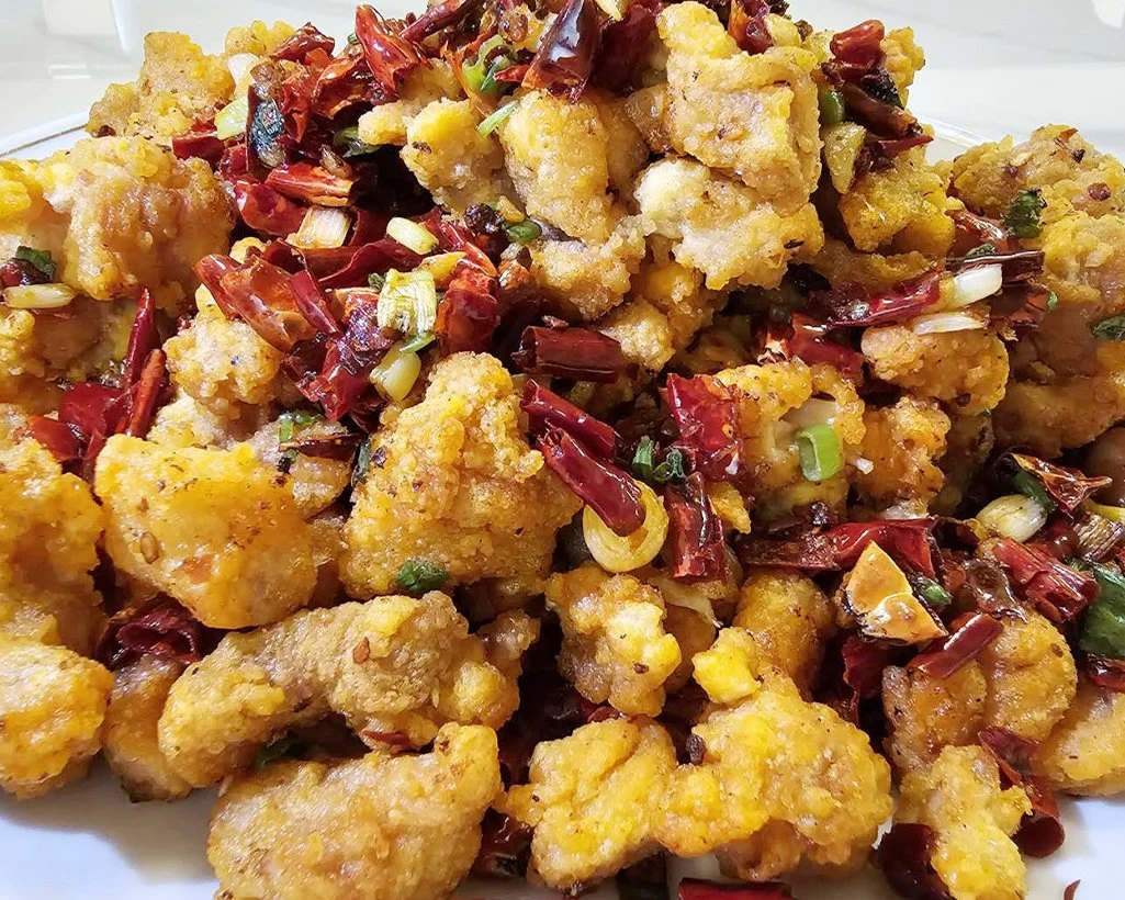 Fried chicken pieces topped with chopped green onions and dried red chili peppers.