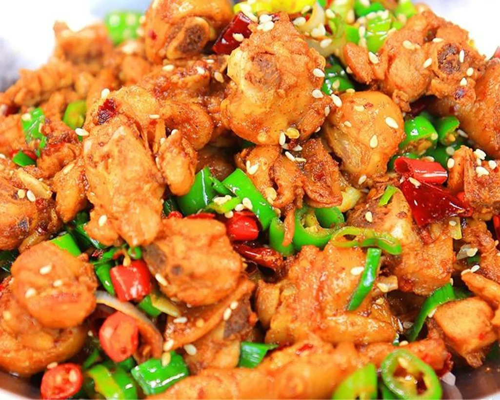 Close-up of stir-fried chicken with green and red chili peppers, garnished with sesame seeds.