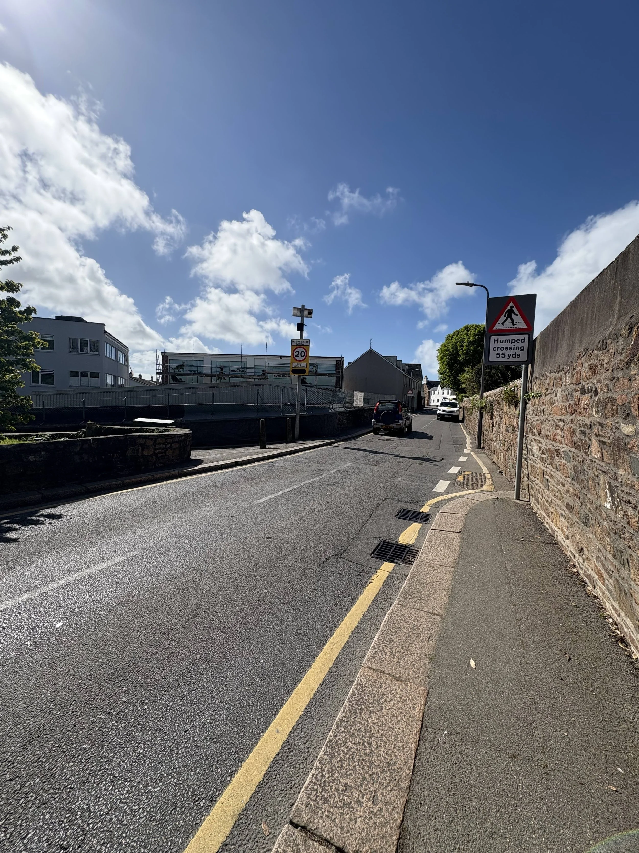 A streetview of St Helier North. There are road signs including a 20 mph speed limit and a humped crossing warning 55 yards ahead. Several cars are parked or driving along the street.