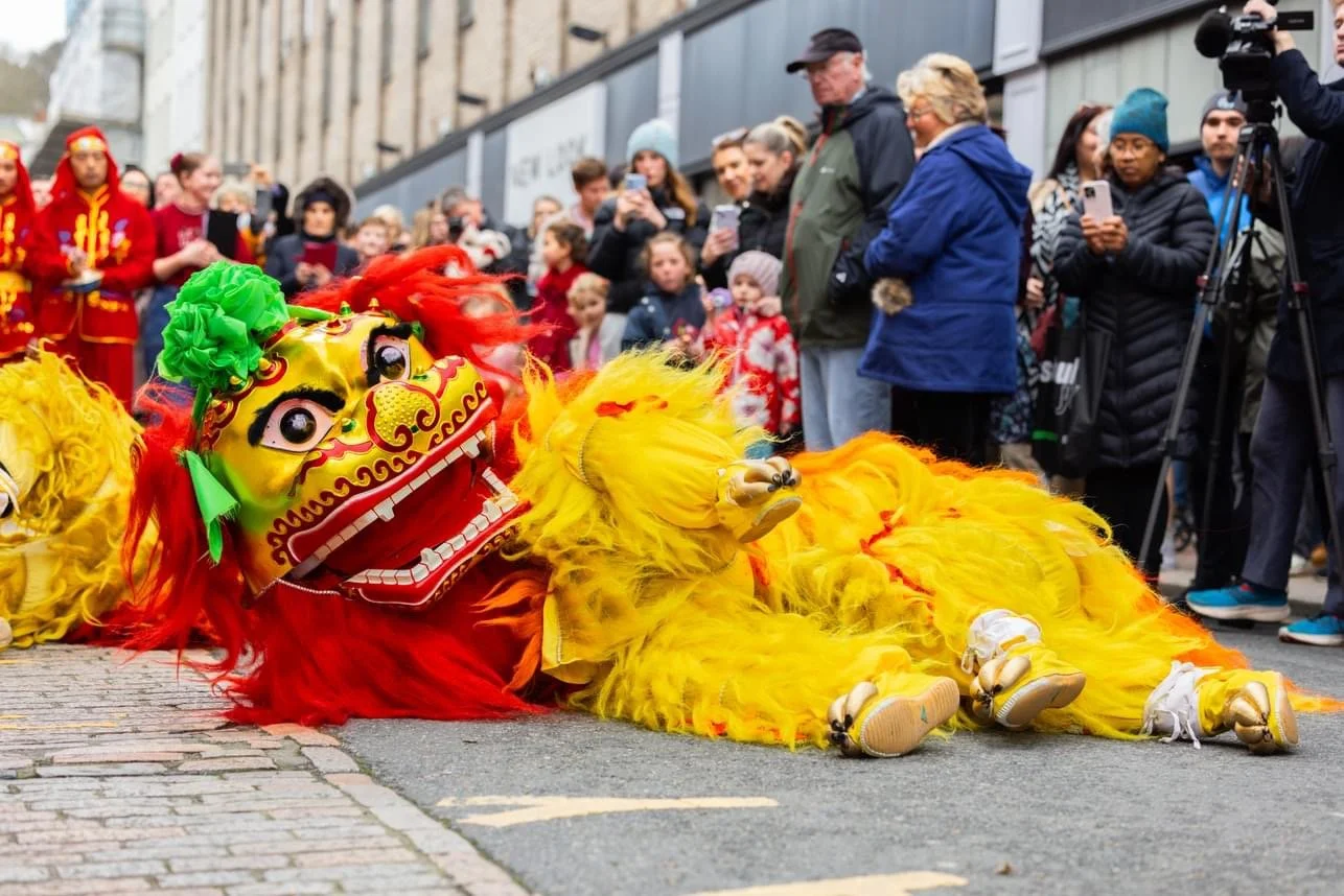 Colorful lion dance costume lying on street during parade with onlookers taking photos