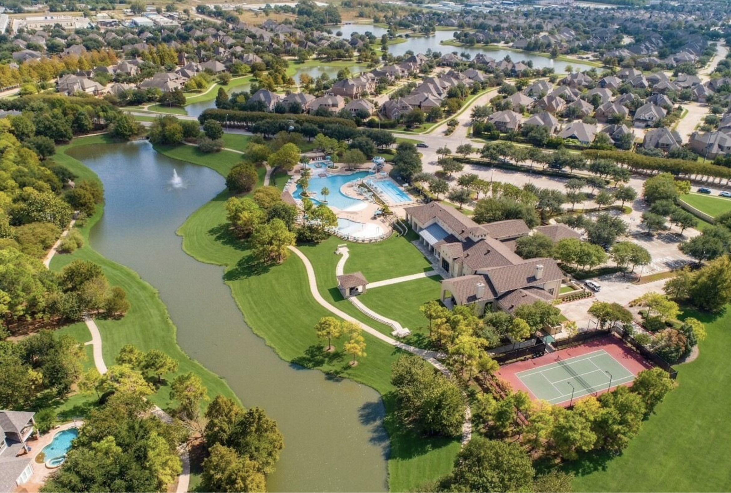 Aerial view of a residential community with houses, a lake, parks, and a swimming pool.