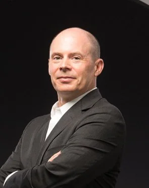 Business professional in a gray suit with arms crossed against a black background