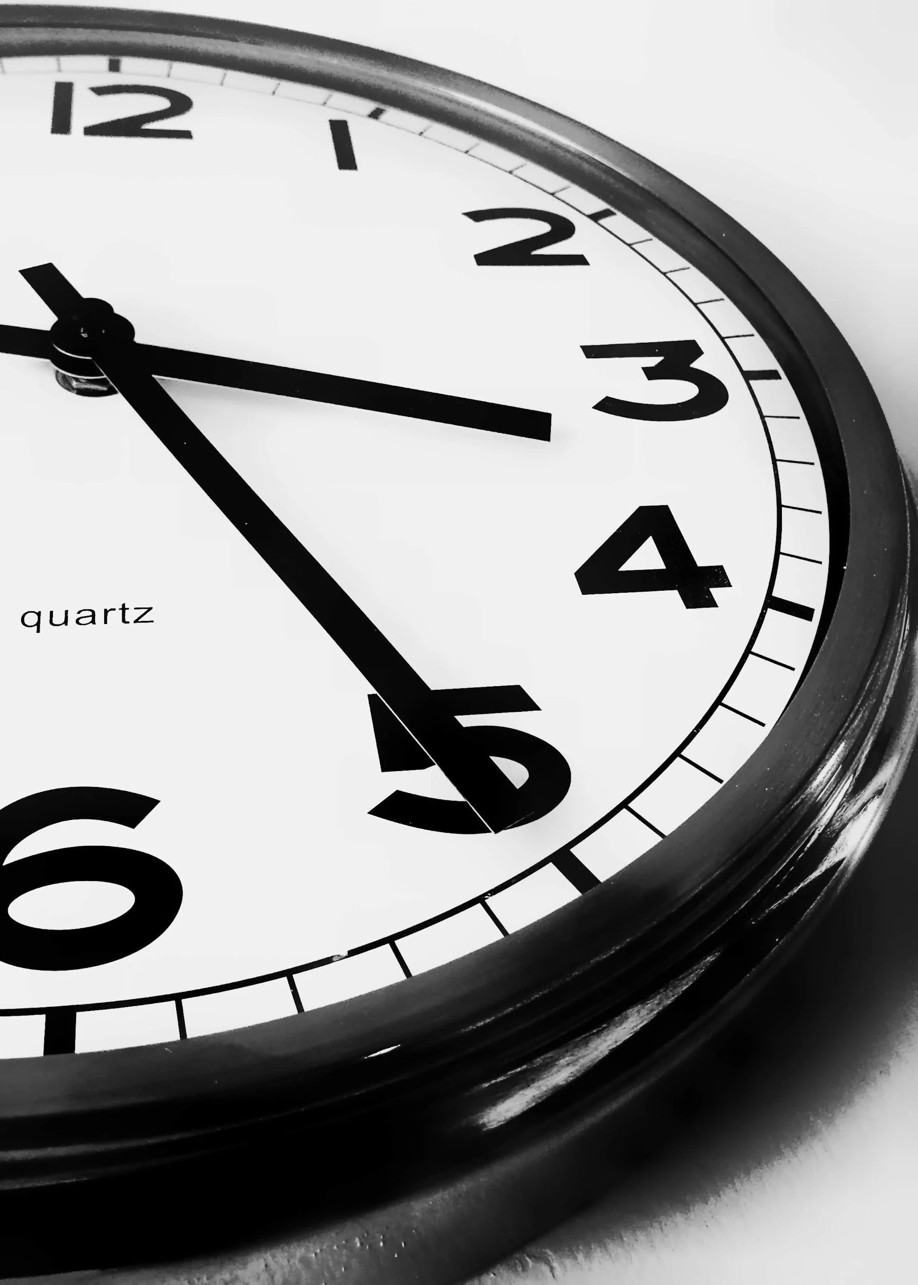 Close-up of an analog clock showing the time as approximately 2:26, with the word 'quartz' on the clock face, in black and white.