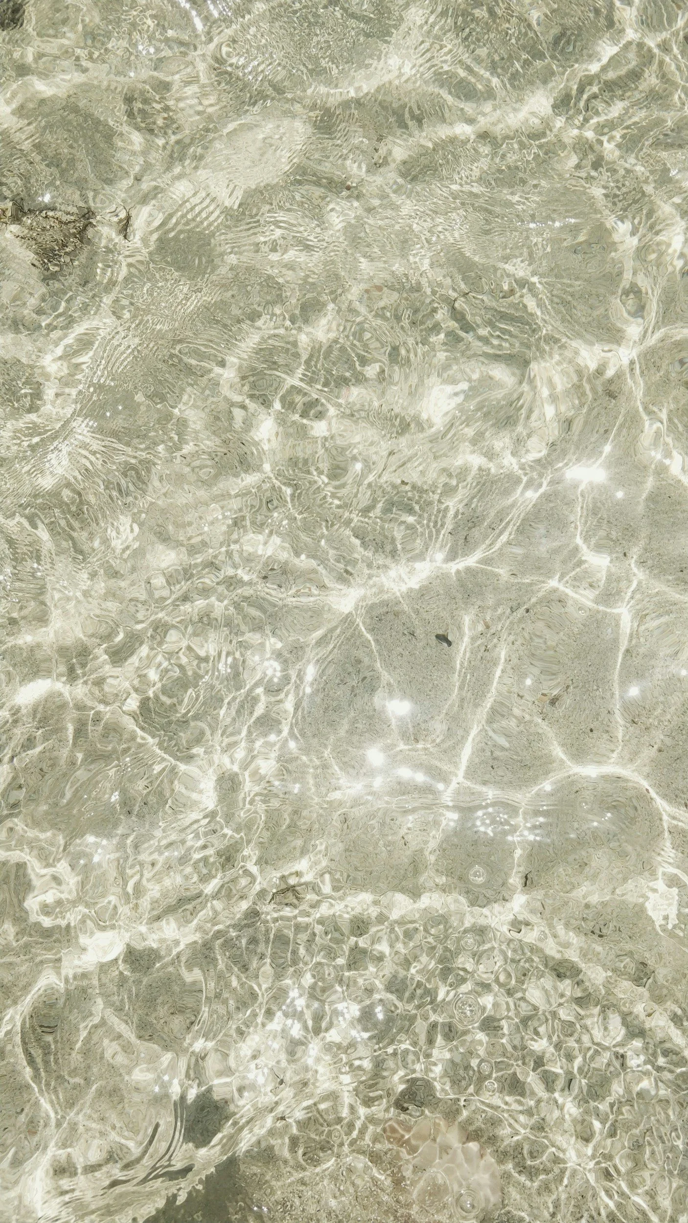 Clear shallow water with ripples on the surface, showing sand and small rocks underneath.