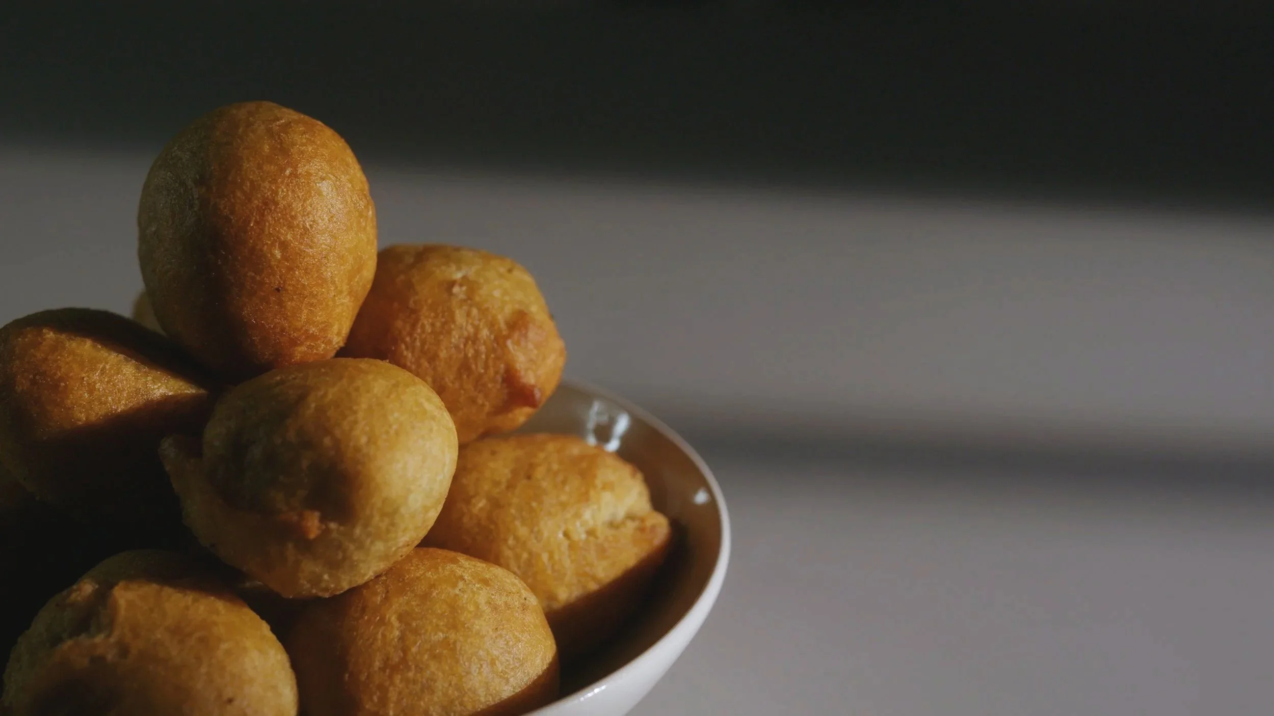 A bowl filled with small, round, fried dough balls on a gray surface with a dark background.
