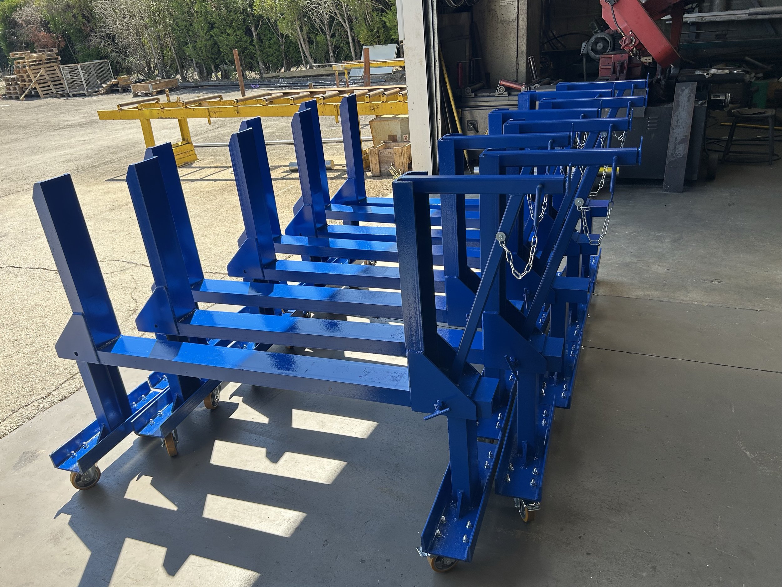 Chariots de manutention bleus alignés dans un espace de stockage extérieur, avec un fond de végétation et des palettes en bois.