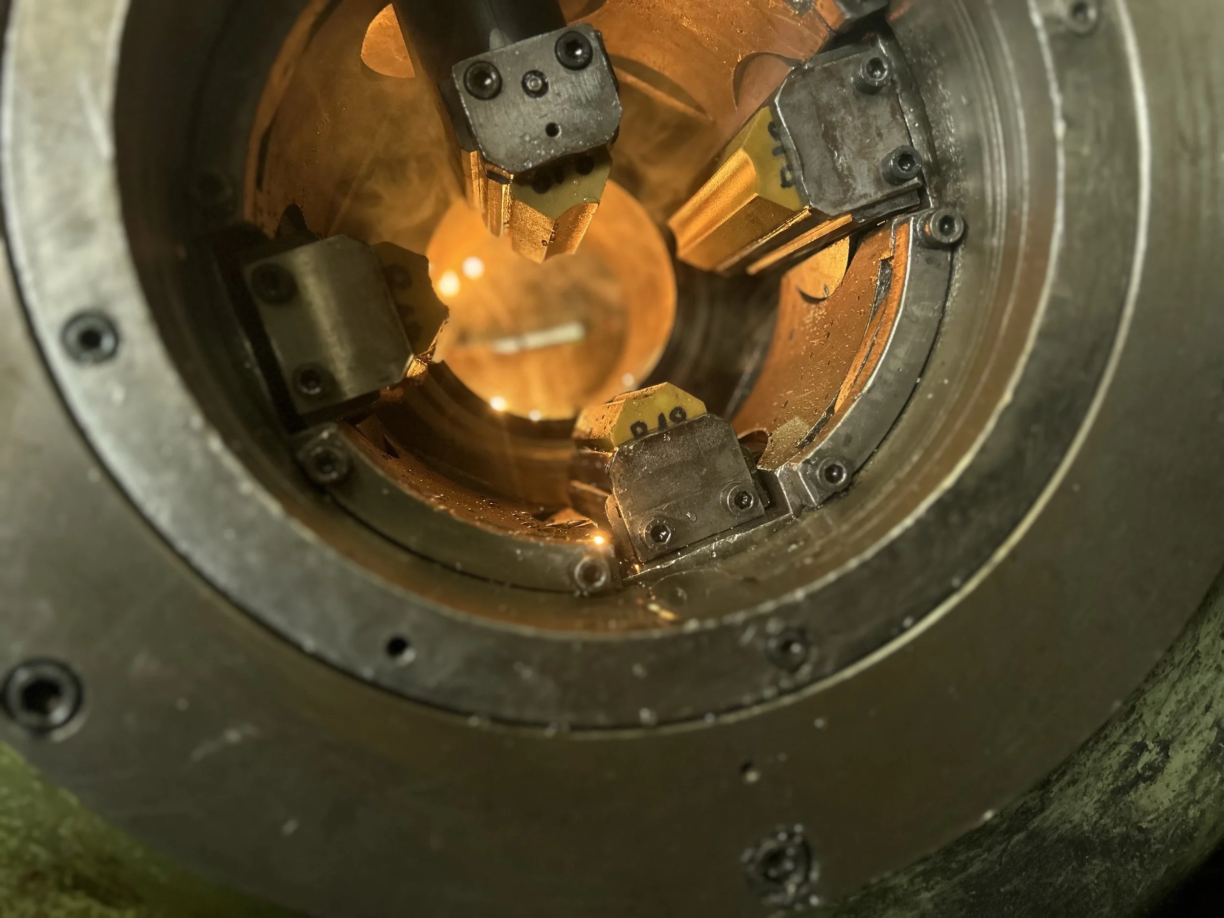 Vue à l'intérieur d'un mécanisme industriel ou d'une machine, avec des pièces métalliques disposées en cercle, enchevêtrées avec des éléments colorés, notamment des composants jaunes et noirs, éclairés par une lumière chaude.