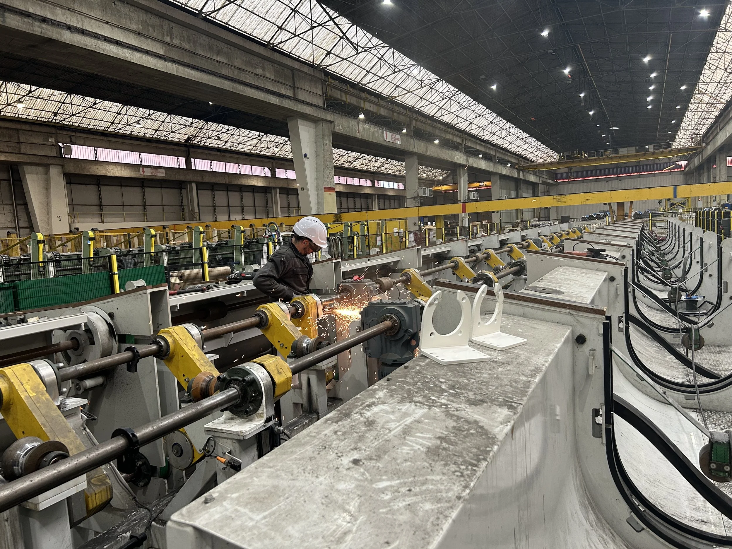 Un ouvrier avec casque de sécurité travaillant dans une usine ou un entrepôt avec des machineries industrielles et des structures métalliques.