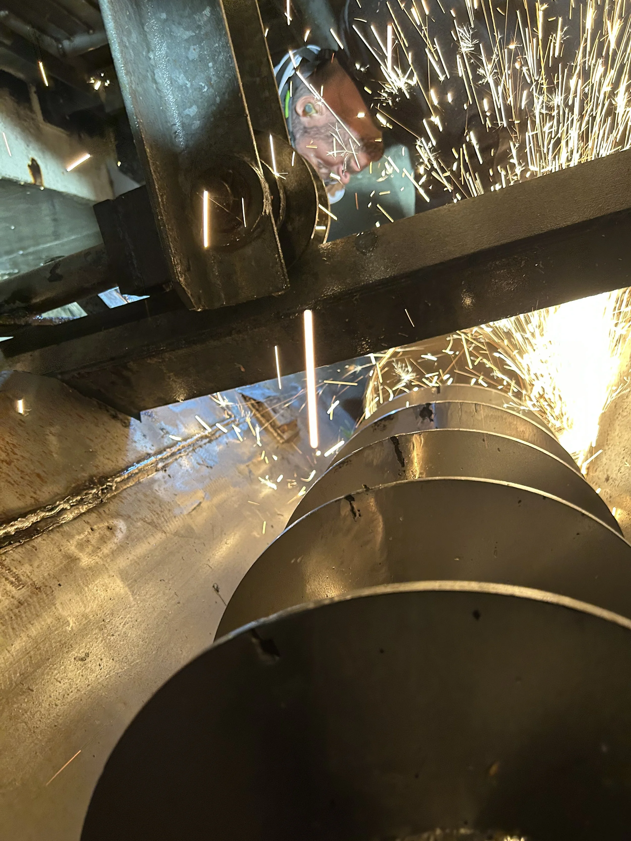 Un métallurgiste utilisant une machine de coupe ou de soudage, produisant des étincelles, avec une personne portant des lunettes de protection, dans un atelier industriel.