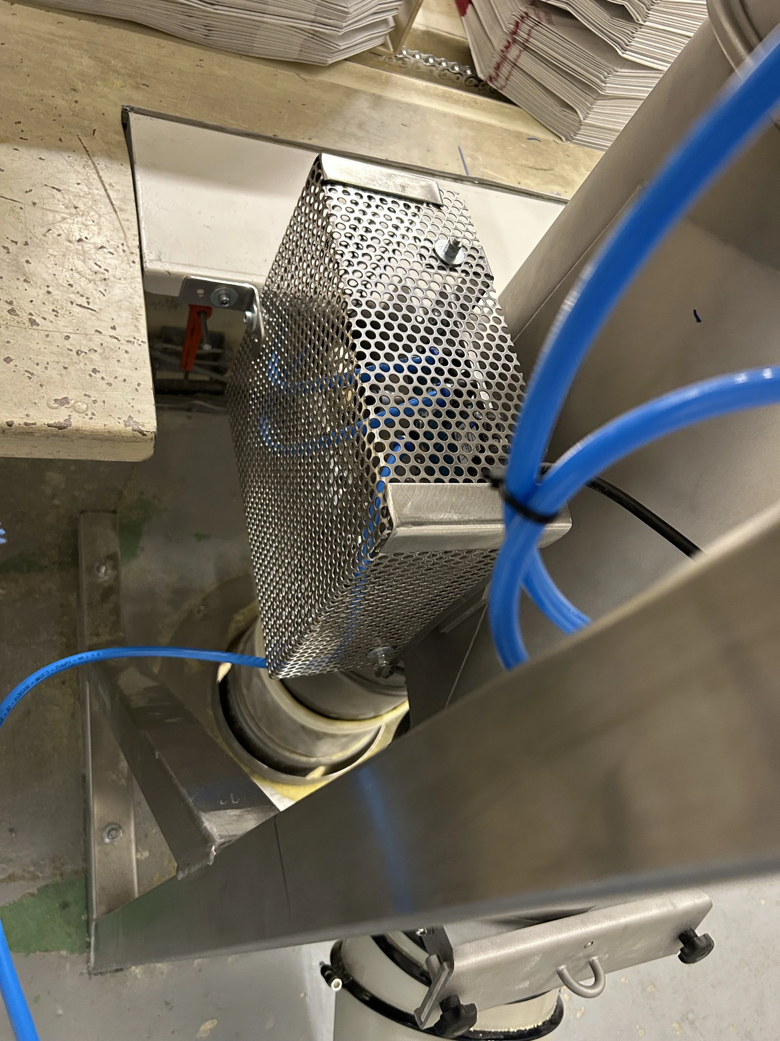 Machine de fabrication industrielle en acier avec un filtre métallique perforé, des câbles bleus et un indicateur rouge, probablement dans une usine ou un laboratoire.
