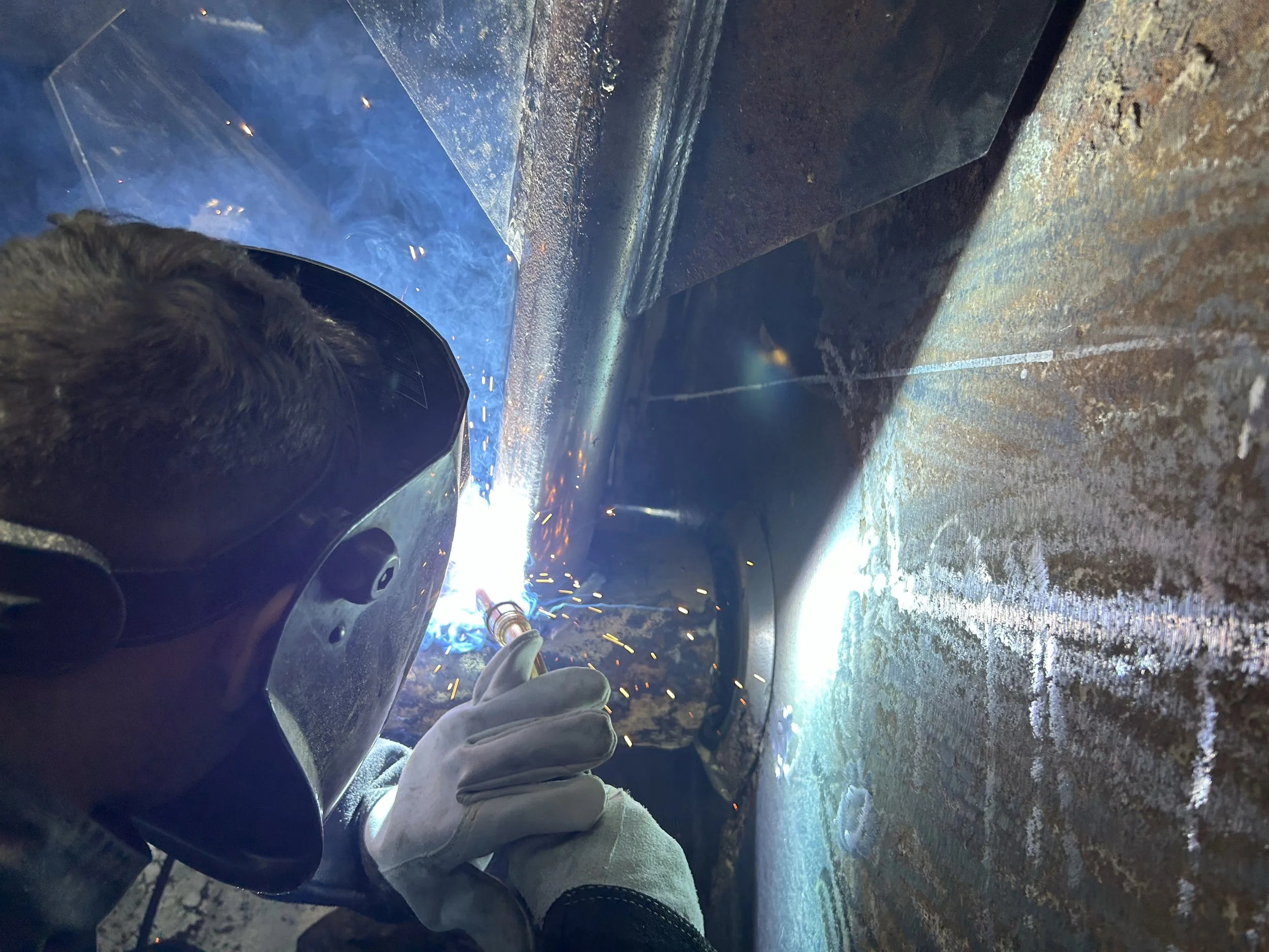 Soudure à l'arc en cours avec des étincelles et des jetons de métal en fusion dans un atelier, vue partielle avec une personne portant un équipement de protection.
