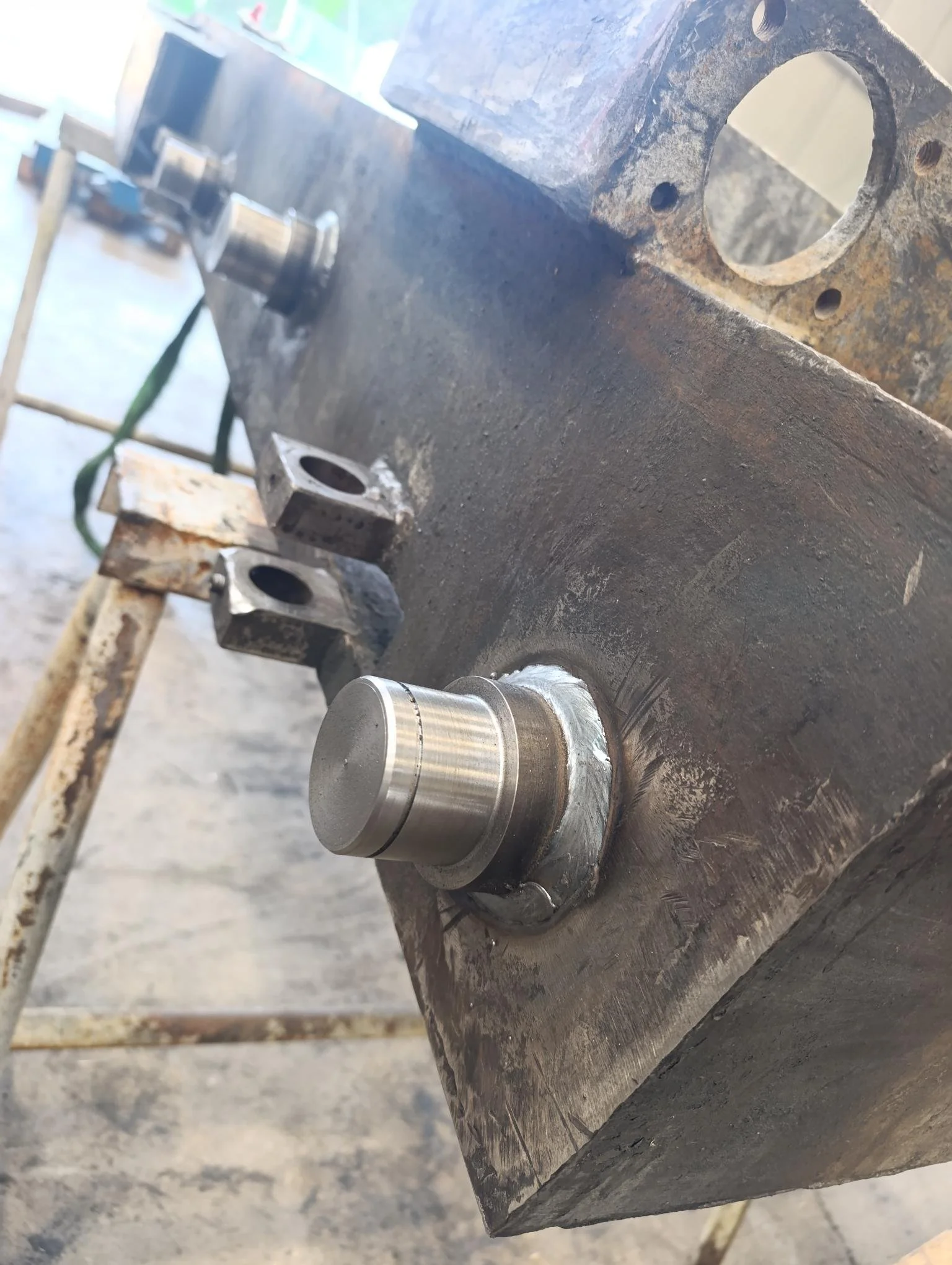 Une pièce mécanique en métal fixée à une surface en métal, avec d'autres composants métalliques visibles en arrière-plan.