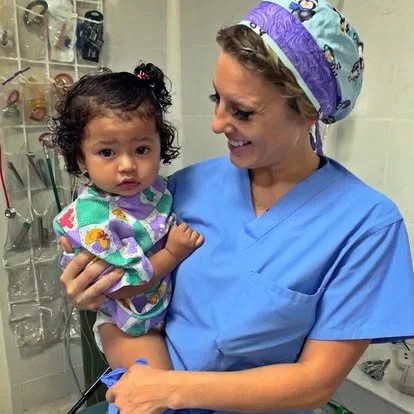A woman in scrubs holding a young girl in a hospital or clinic setting.