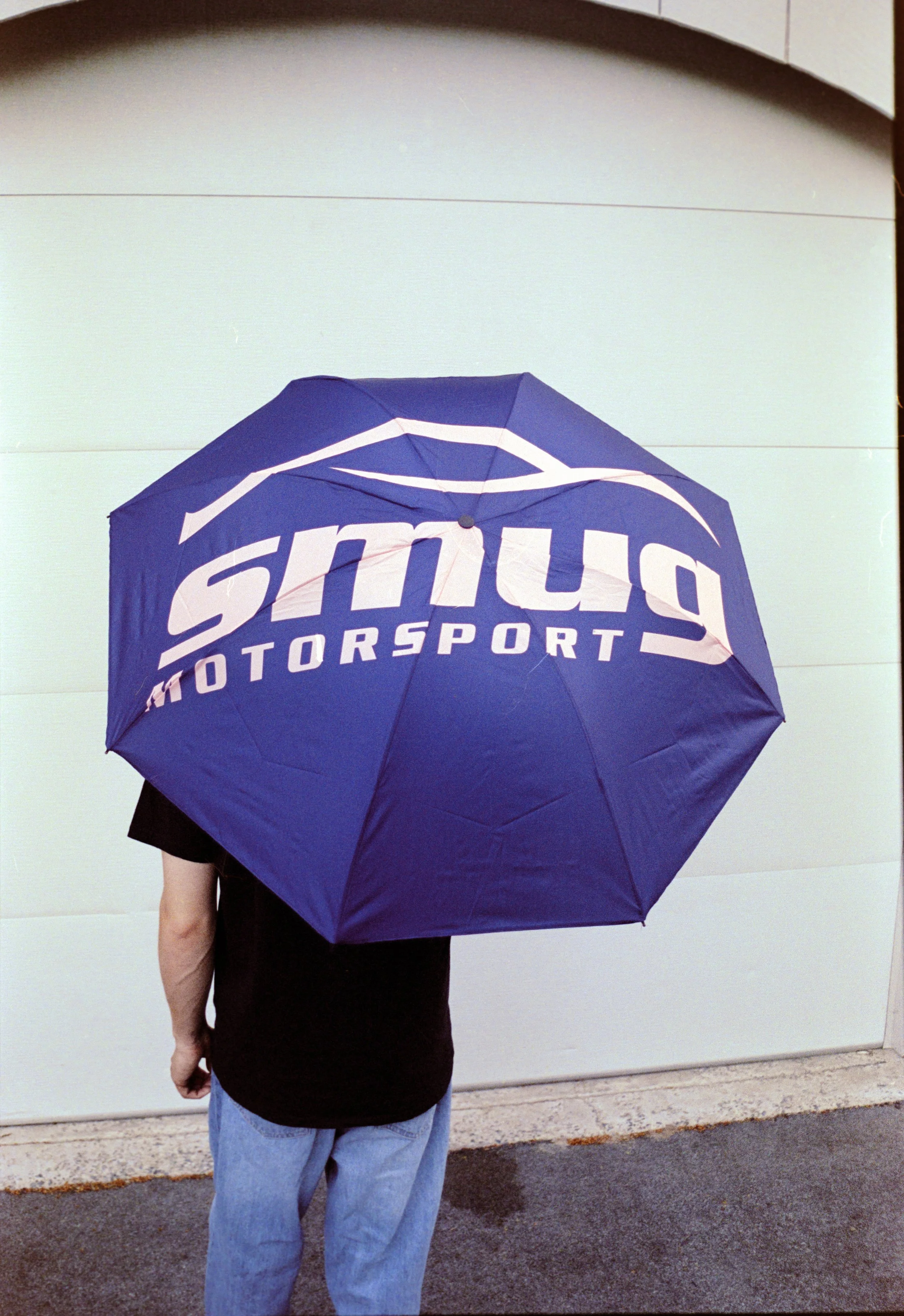 Person holding a blue umbrella with the logo of 'SMU Motorsports' visible on it.