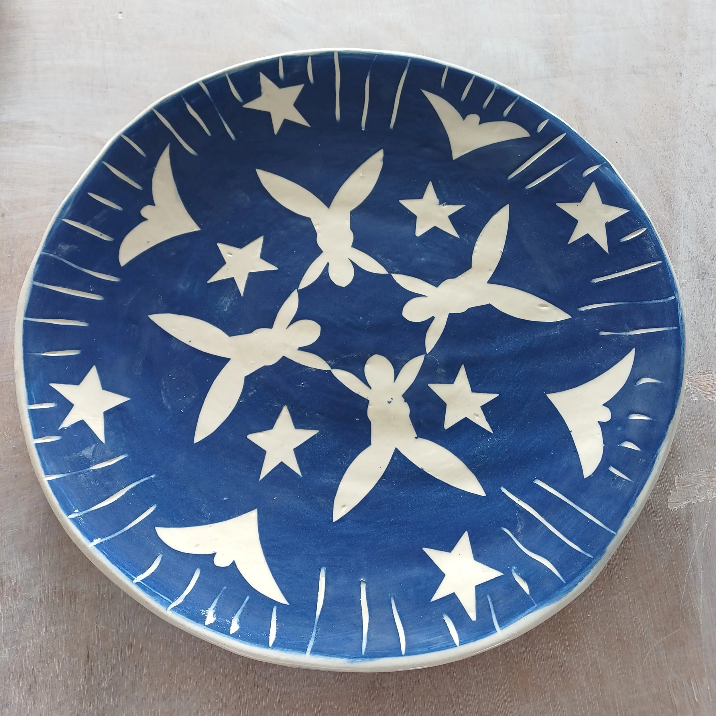 Blue ceramic plate with white star and figure patterns and decorative lines.