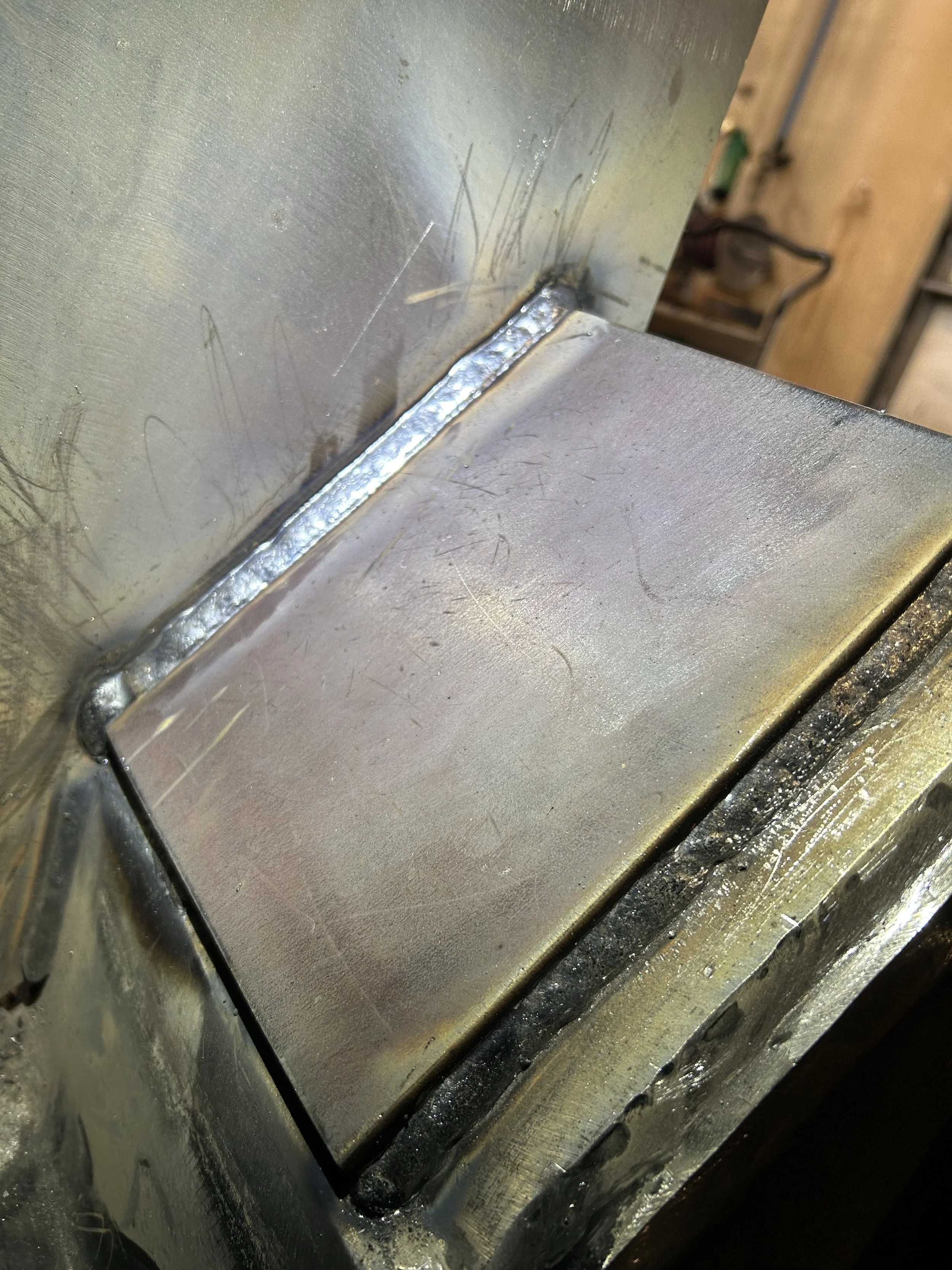 Close-up of a metal surface with a welded joint, showing shiny weld beads and surrounding scratches and marks.
