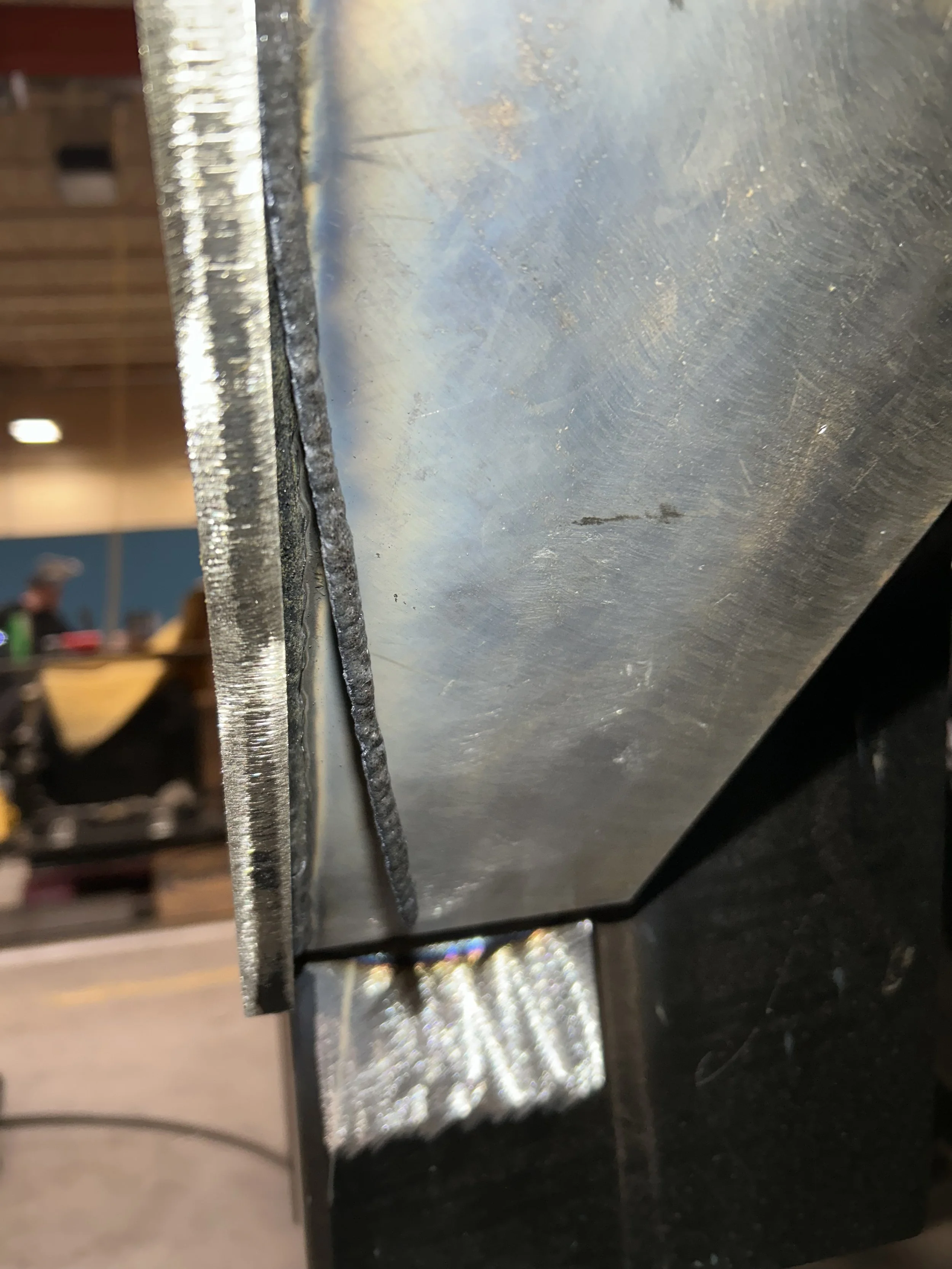 Close-up of a metal object, with soldered joint, reflecting light, in an industrial or workshop setting.