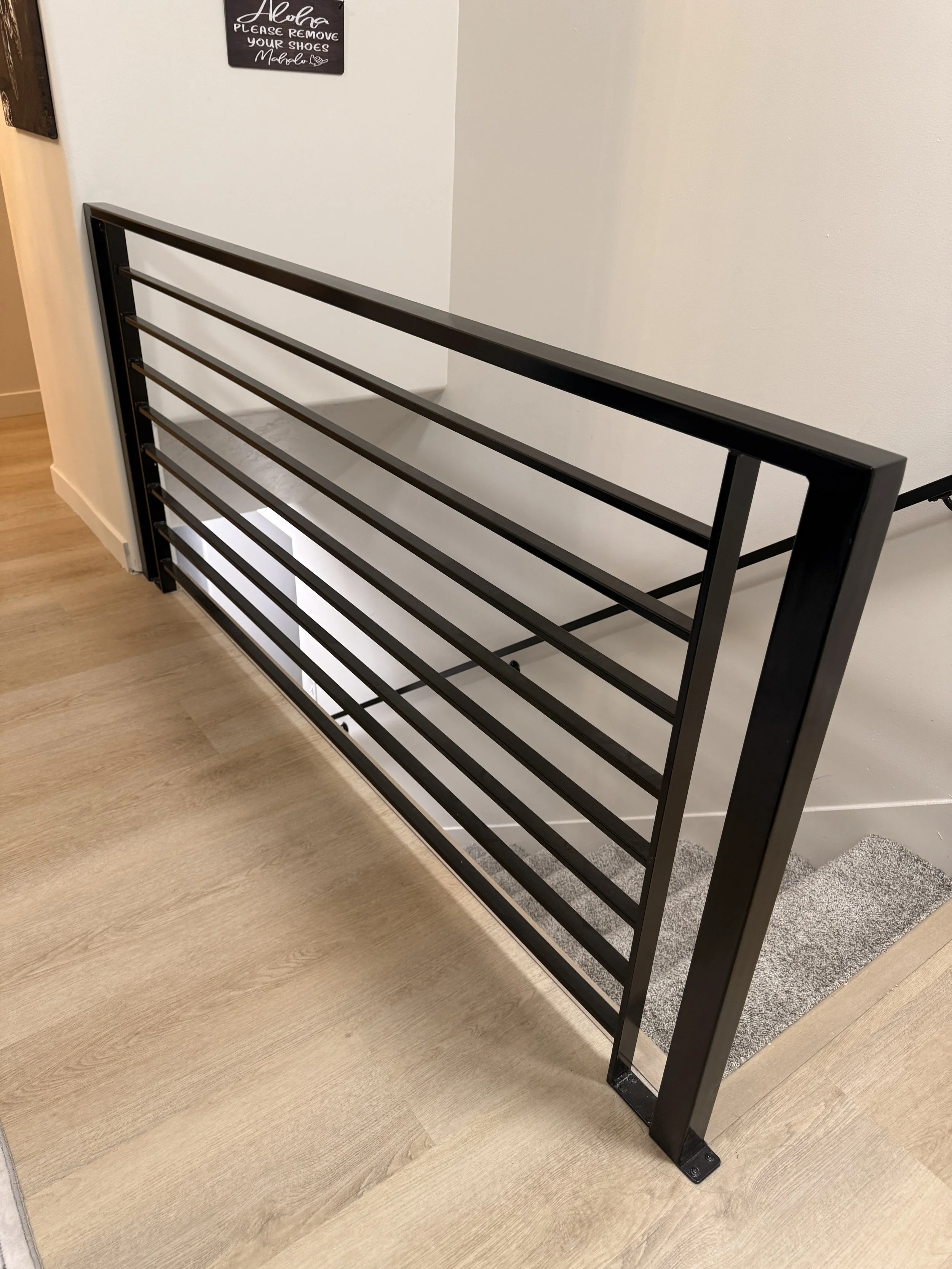 Black metal shoe rack against a white wall, with a small mat in front of it on a light wooden floor.