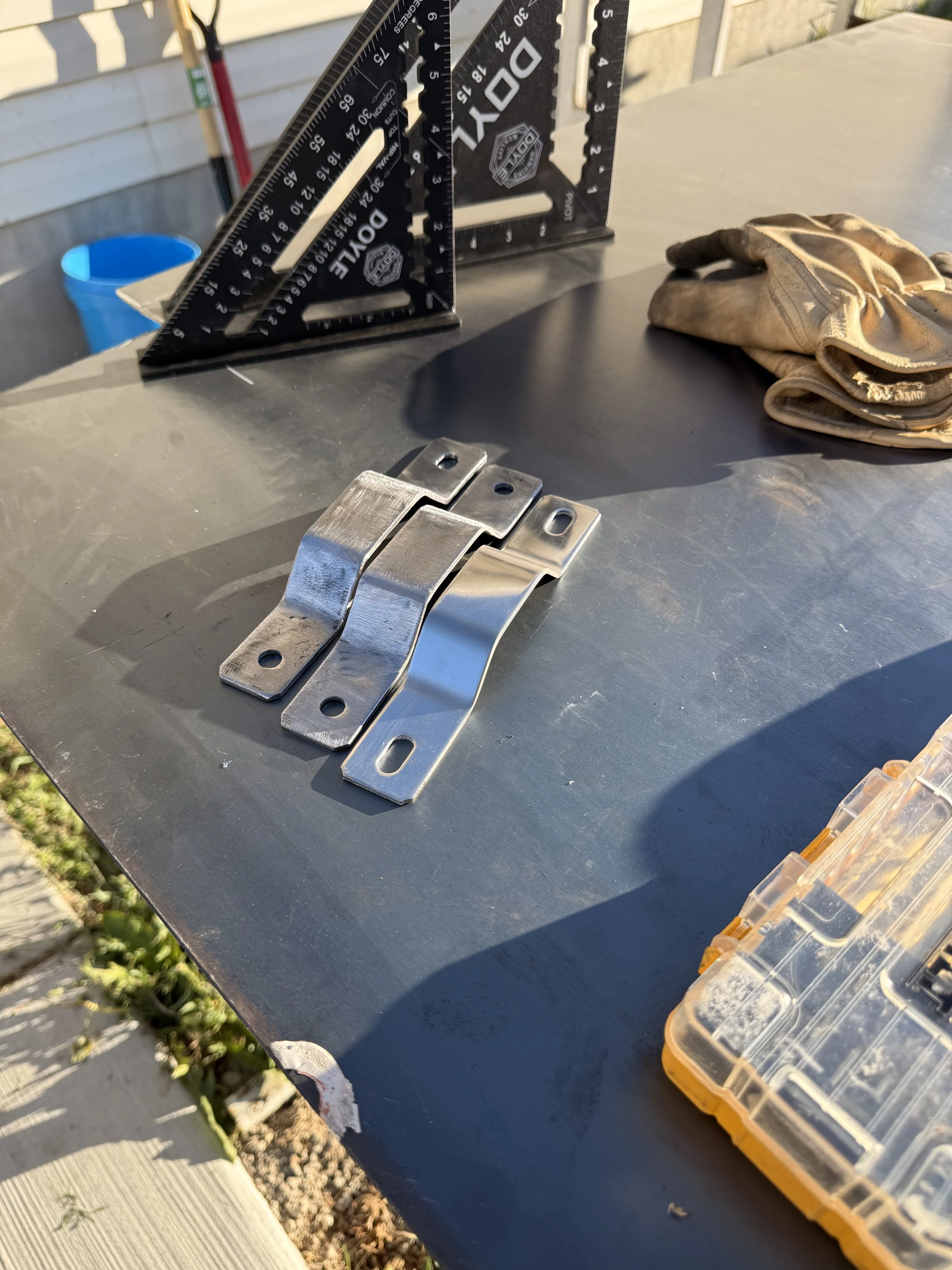 A workbench with metal brackets, a pair of carpenter's triangles, a pair of gloves, and a plastic container with fasteners inside.