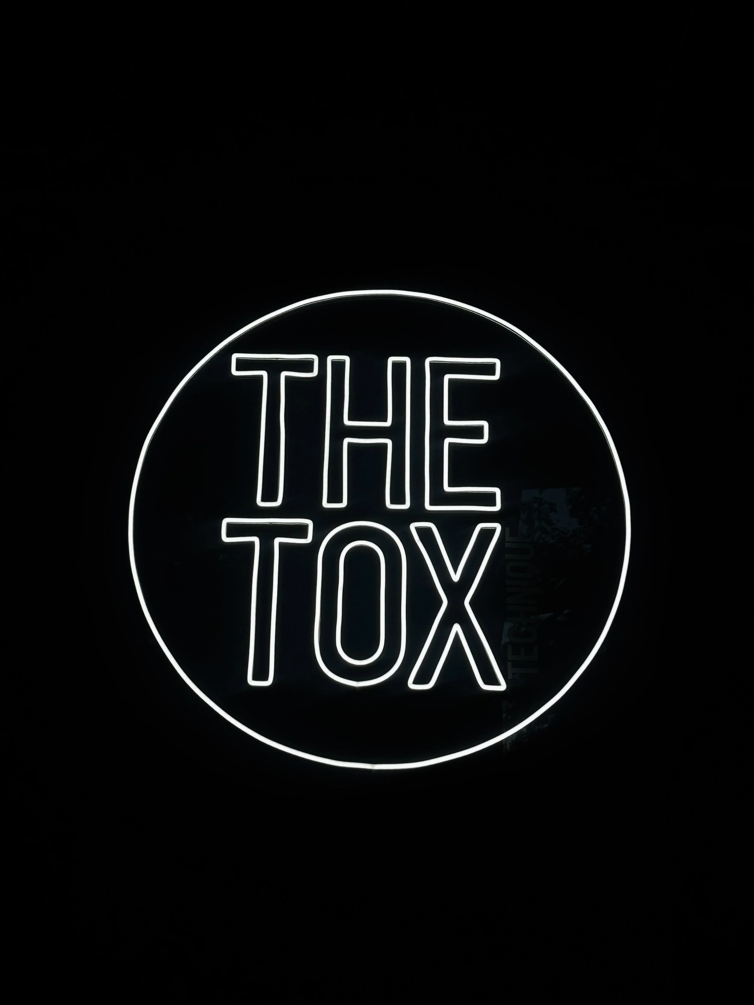 Neon sign with the text "THE TOX" in white, circular shape with a black background.