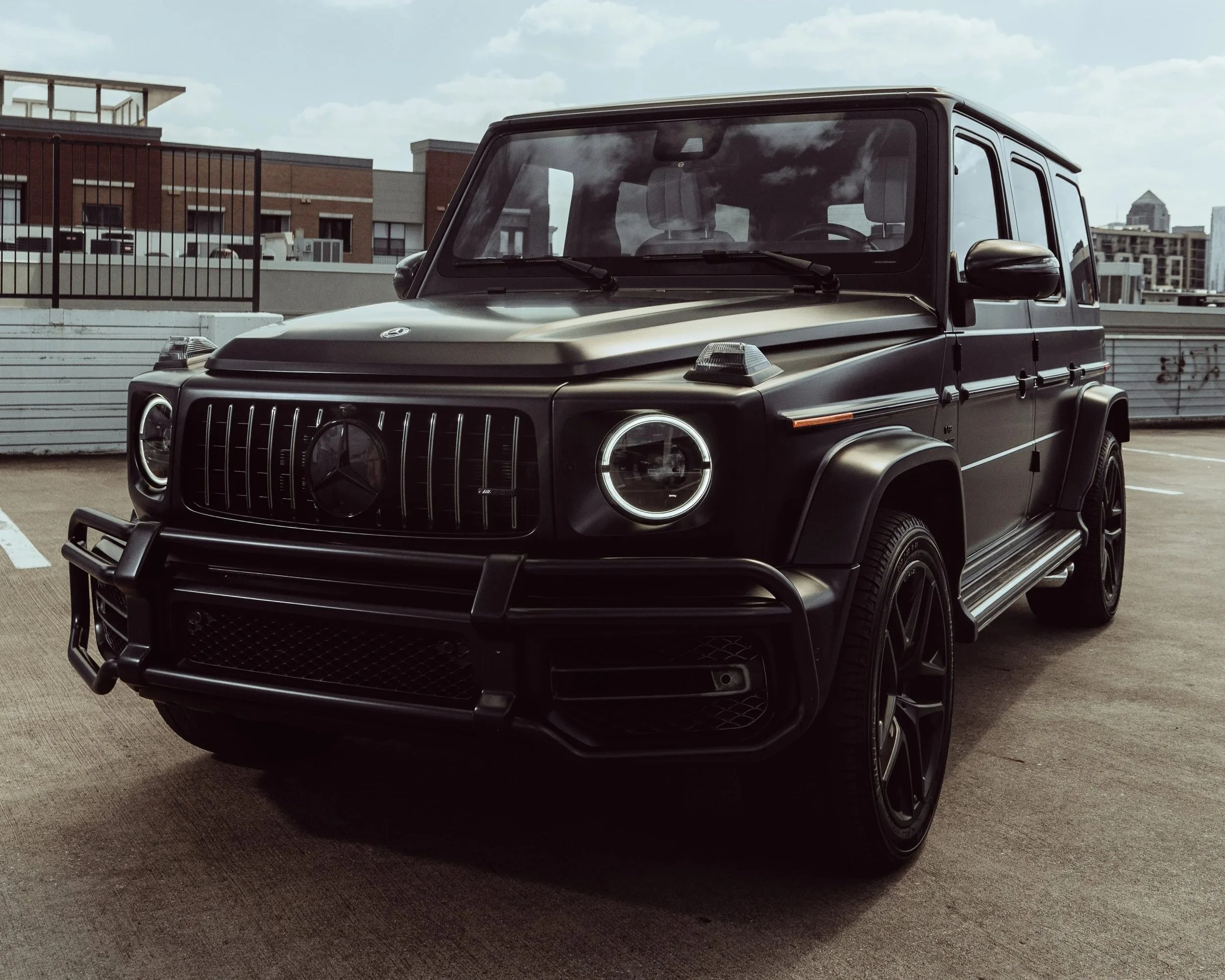 Black Mercedes-Benz G-Class SUV parked on the rooftop parking lot with a city skyline in the background.