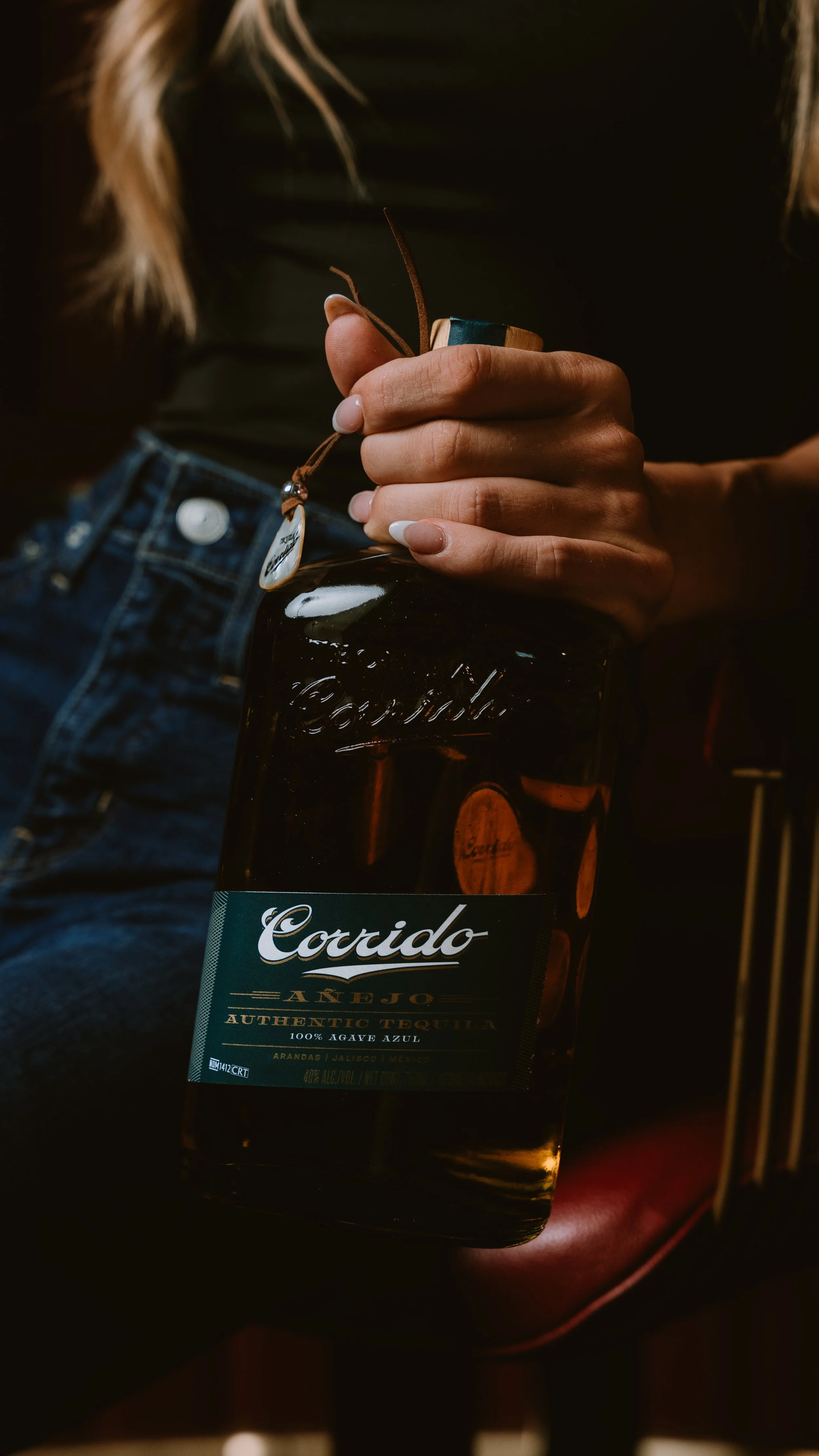 A person holding a bottle of Coccido Añejo tequila with a leather strap attached.