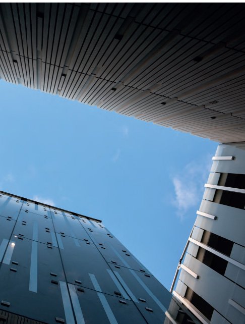 Looking up between modern glass and metal skyscrapers at a clear blue sky.