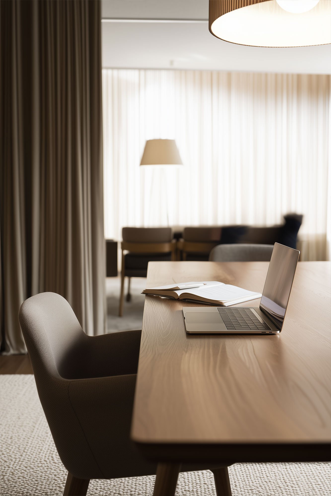 A modern, cozy workspace with a wooden desk, an open laptop, a closed notebook, a gray chair, and natural light filtering through sheer curtains in the background.